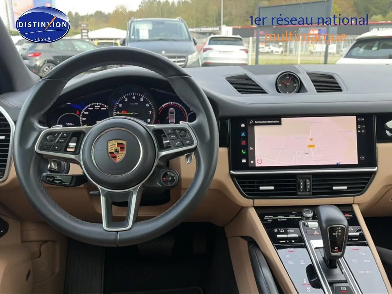 Vue intérieure avant du tableau de bord beige et volant cuir noir du Porsche Cayenne hybride avec écran tactile et levier de vitesse.