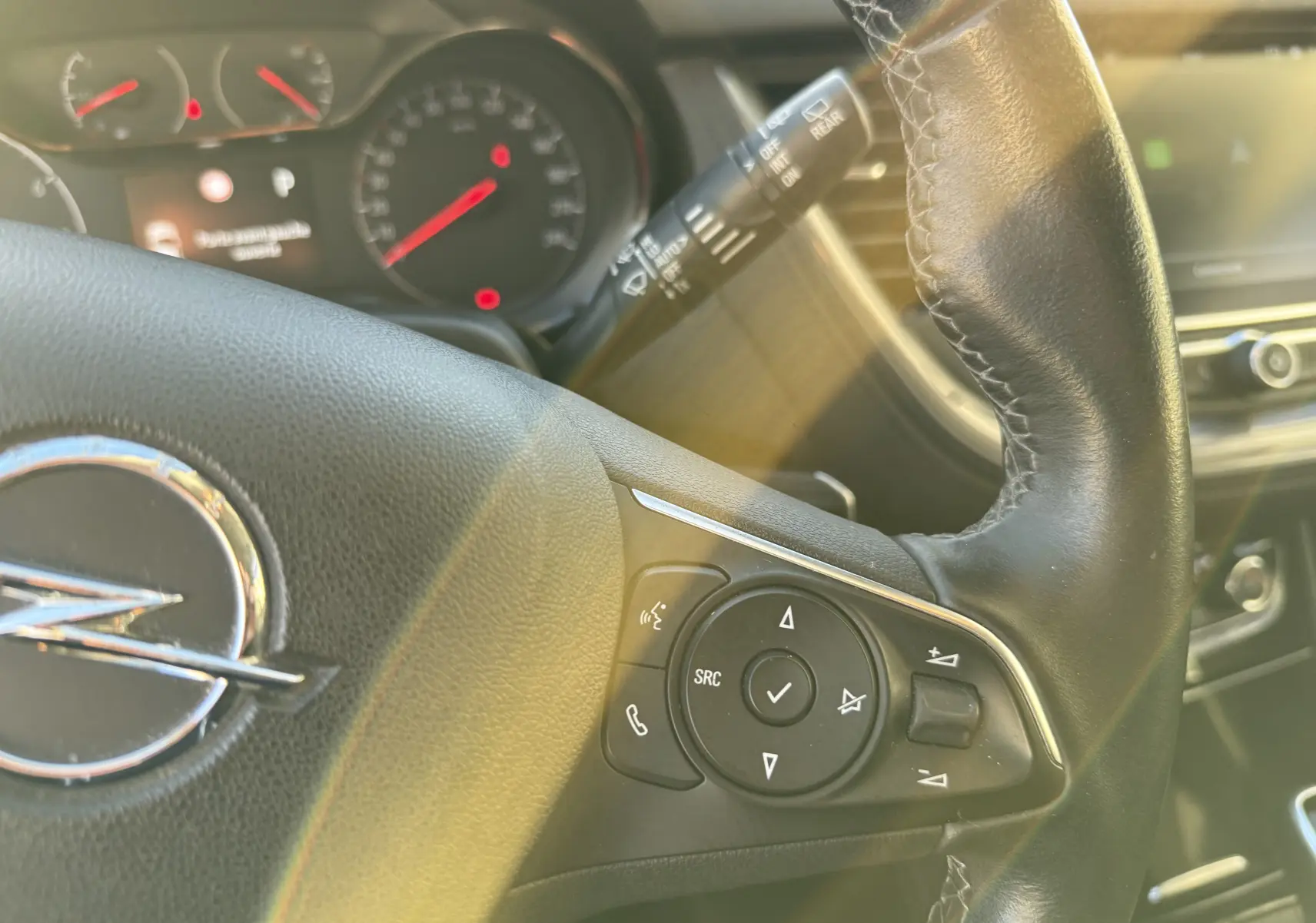 Gros plan sur le volant en cuir noir de l'Opel Grandland X 2019, avec commandes intégrées et tableau de bord flou en arrière-plan.