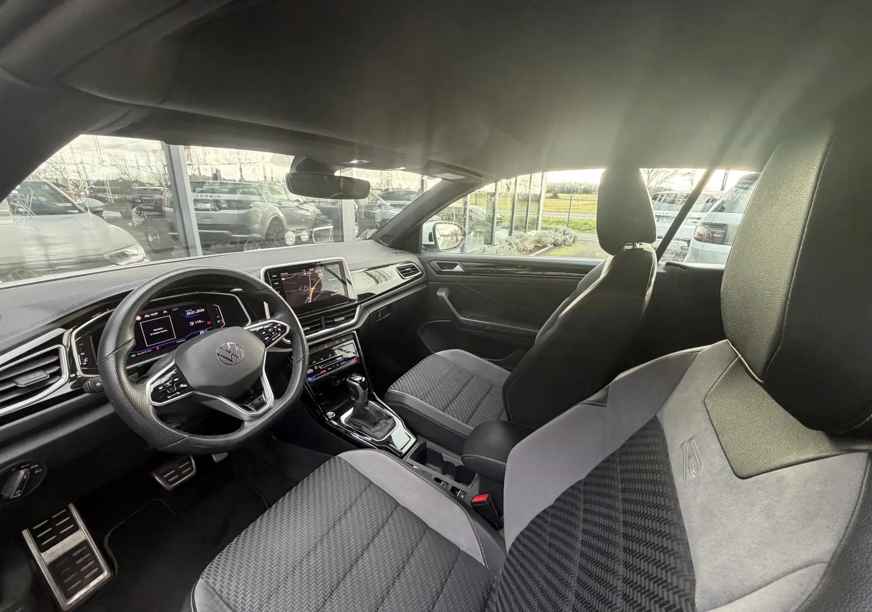 Vue intérieure côté conducteur du Volkswagen T-Roc Cabriolet 2022, sièges R-Line en tissu noir et gris avec volant multifonction.