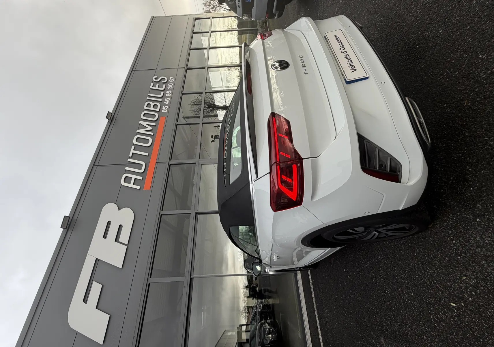 Vue 3/4 arrière droite d'un Volkswagen T-Roc Cabriolet blanc 2022 avec toit noir, garé devant un concessionnaire.
