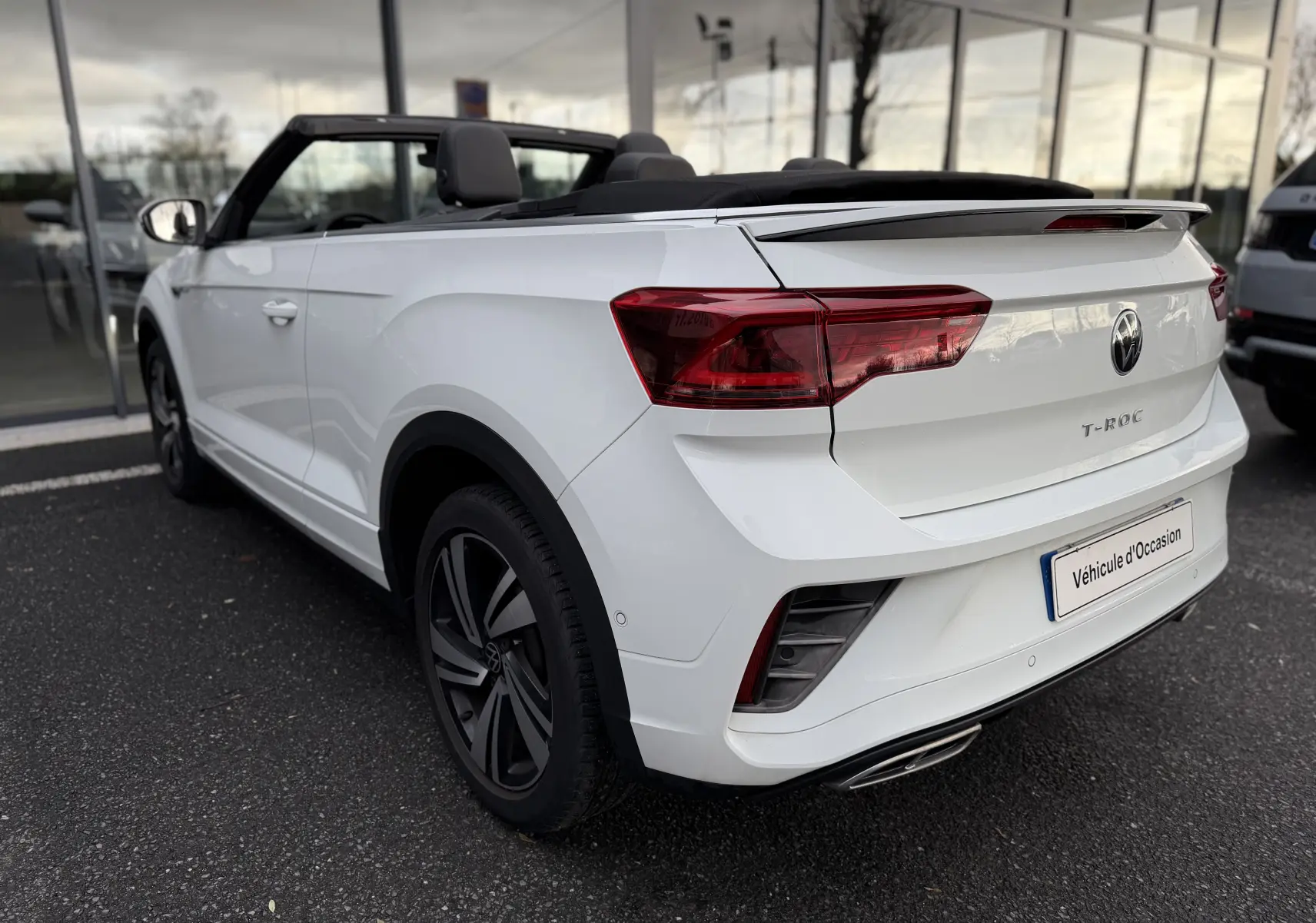Vue 3/4 arrière droite d'un Volkswagen T-Roc Cabriolet blanc 2022 avec toit ouvert et finition R-Line.