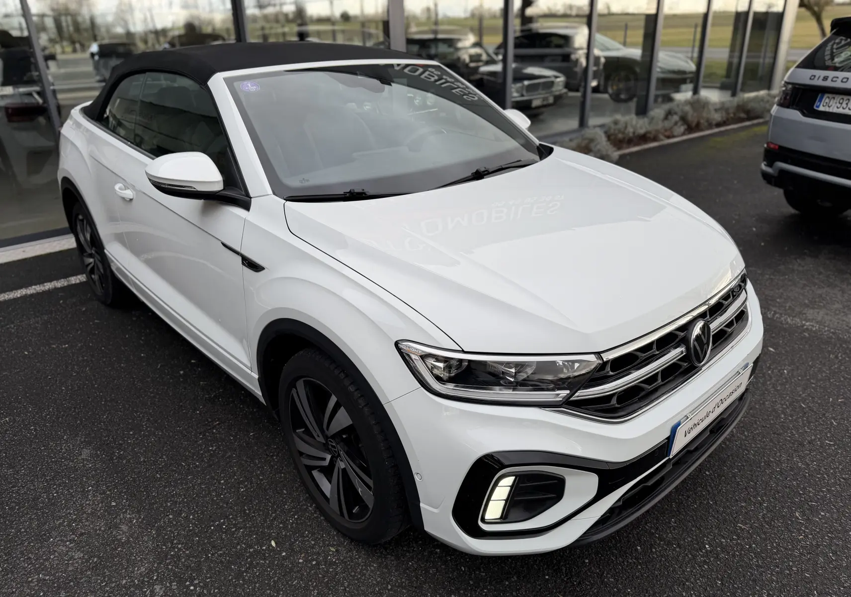Vue 3/4 avant d’un Volkswagen T-Roc Cabriolet blanc 2022 avec toit noir fermé et finition R-Line.