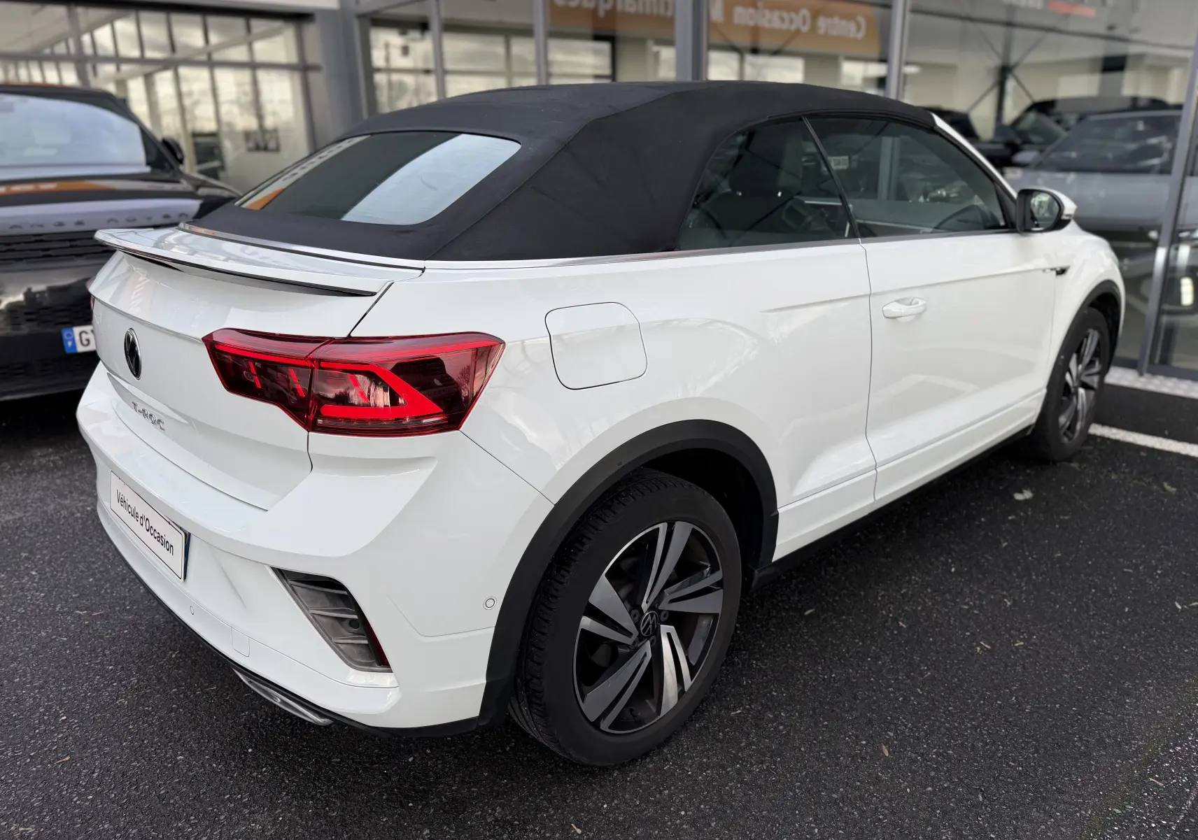Vue 3/4 arrière droite d’un Volkswagen T-Roc Cabriolet blanc avec capote noire et jantes R-Line distinctives.