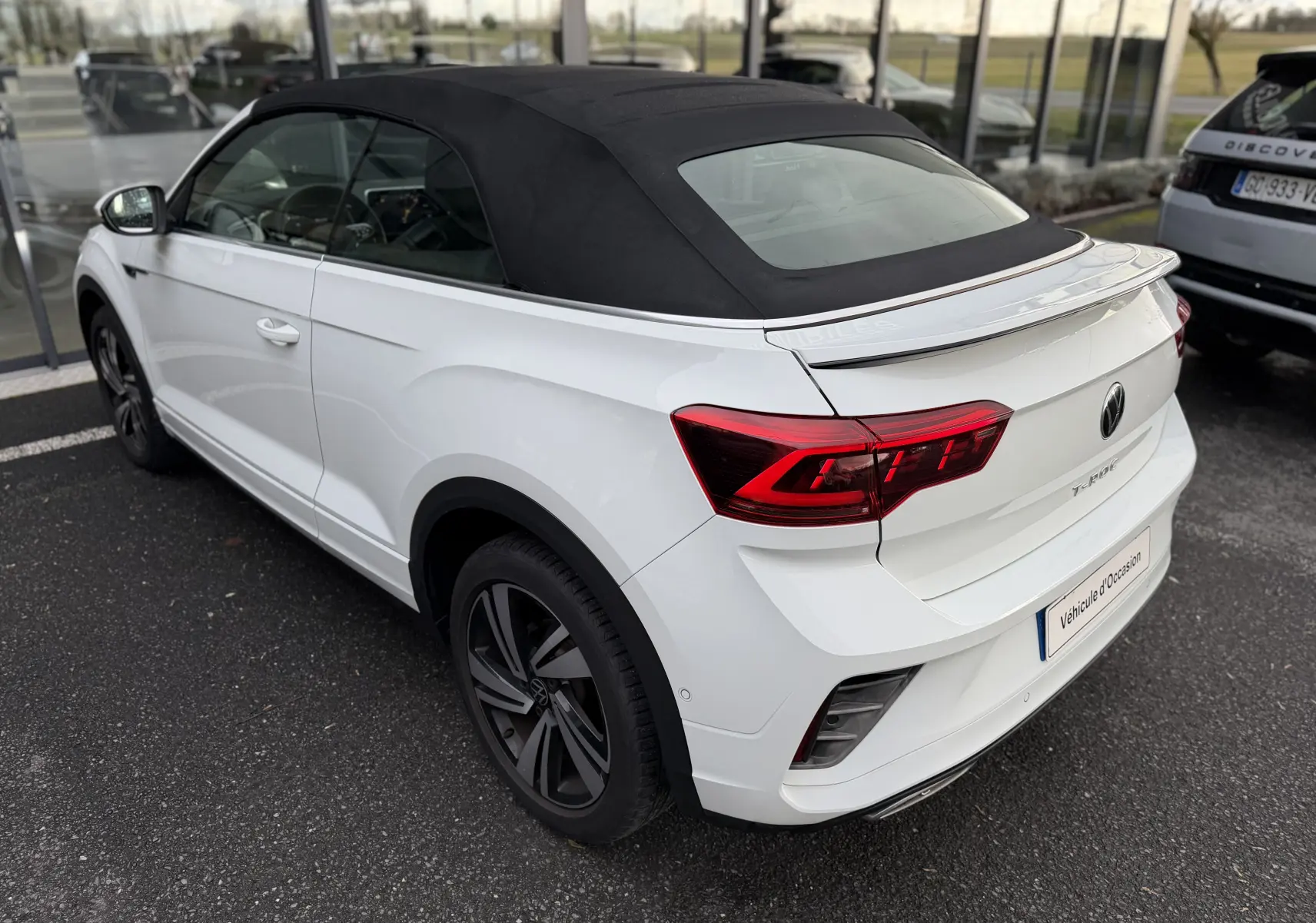 Vue 3/4 arrière droite d’un Volkswagen T-Roc Cabriolet blanc 2022 avec toit souple noir et jantes R-Line.