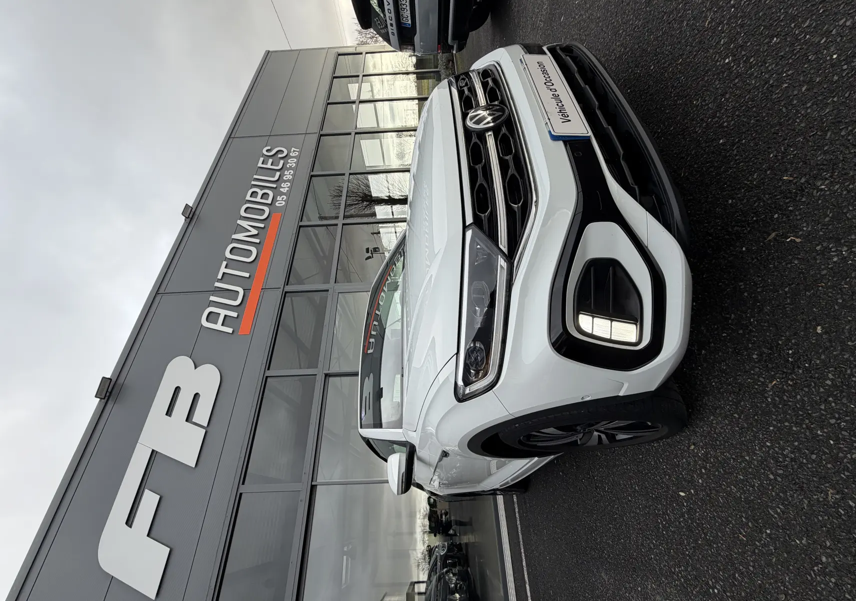 Vue 3/4 avant droit d'un Volkswagen T-Roc Cabriolet blanc 2022 avec finition R-Line devant un showroom.