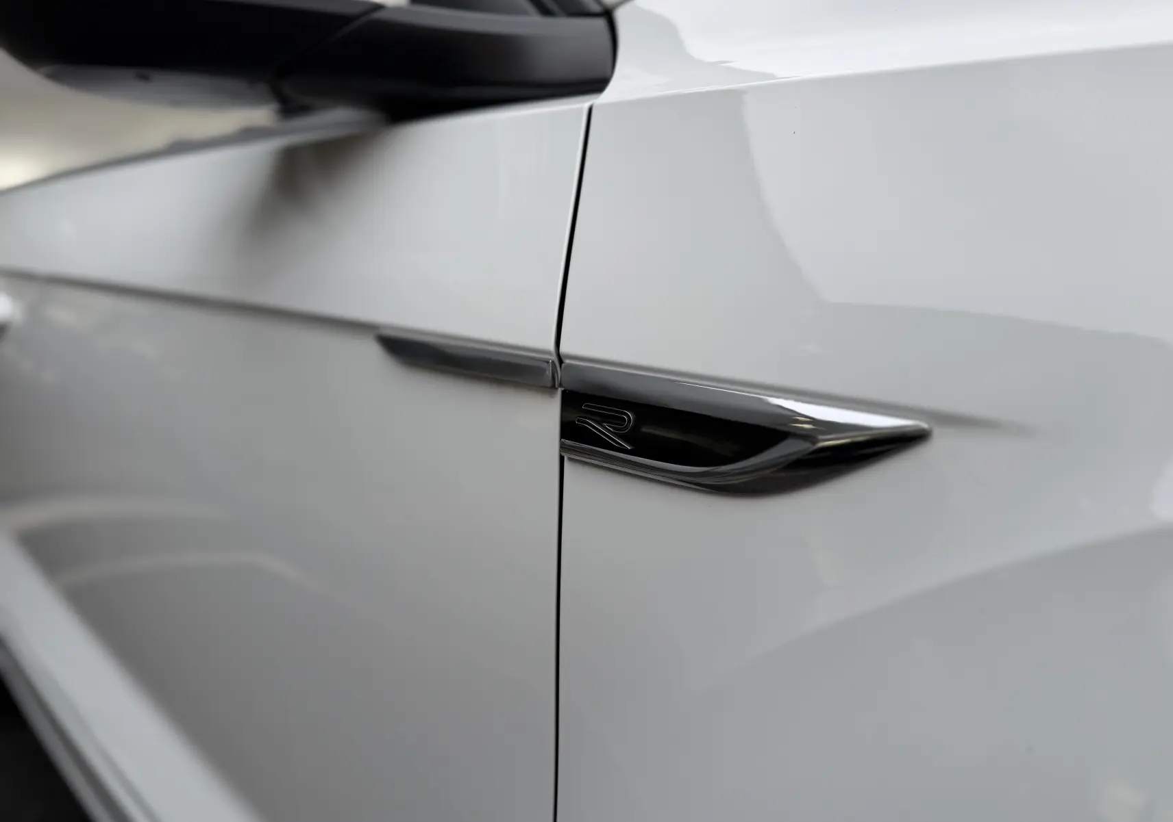 Détail du logo R noir sur la porte côté gauche d’un Volkswagen T-Roc Cabriolet blanc 2022 finition R-Line.