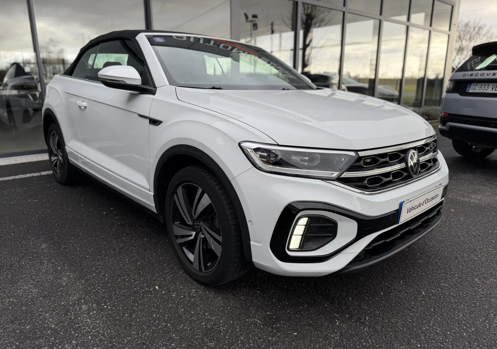 Volkswagen T-Roc Cabriolet blanc vue 3/4 avant droit, capote noire fermée et jantes R-Line distinctives.