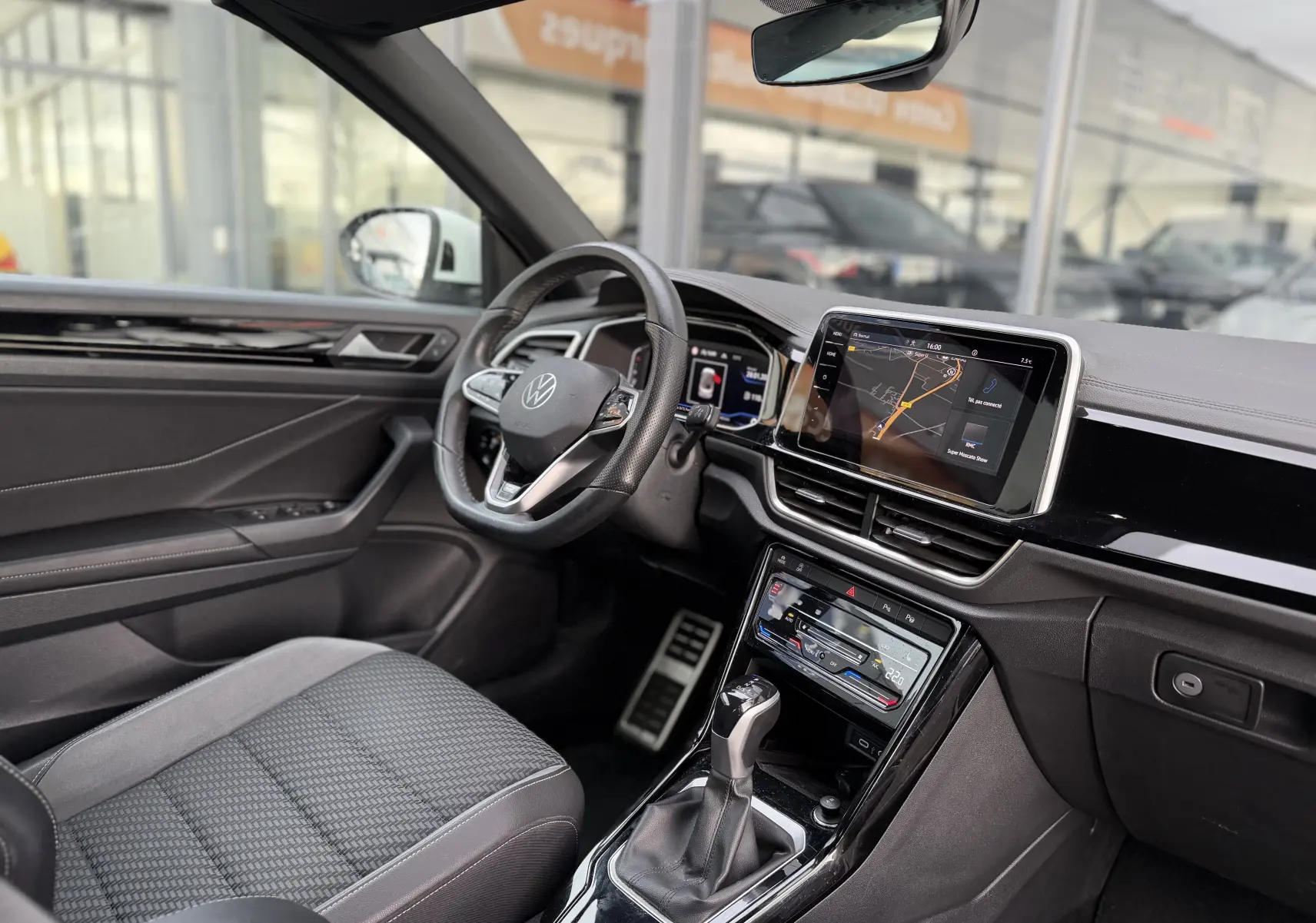 Vue intérieure côté conducteur du Volkswagen T-Roc Cabriolet blanc 2022, avec tableau de bord numérique et écran tactile central.