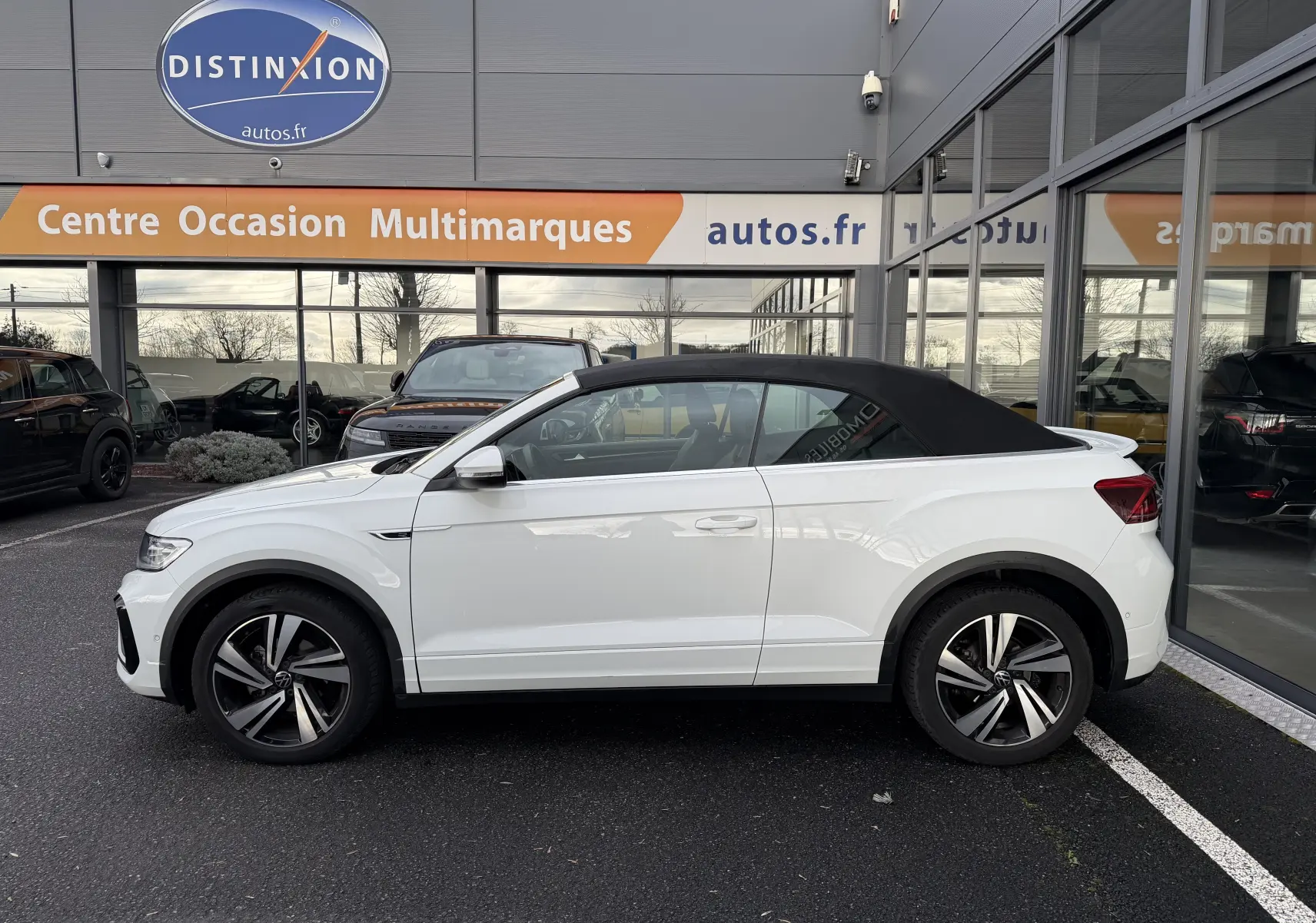 Vue de profil côté gauche d'un Volkswagen T-Roc Cabriolet blanc avec toit noir en position fermée, version R-Line 2022.