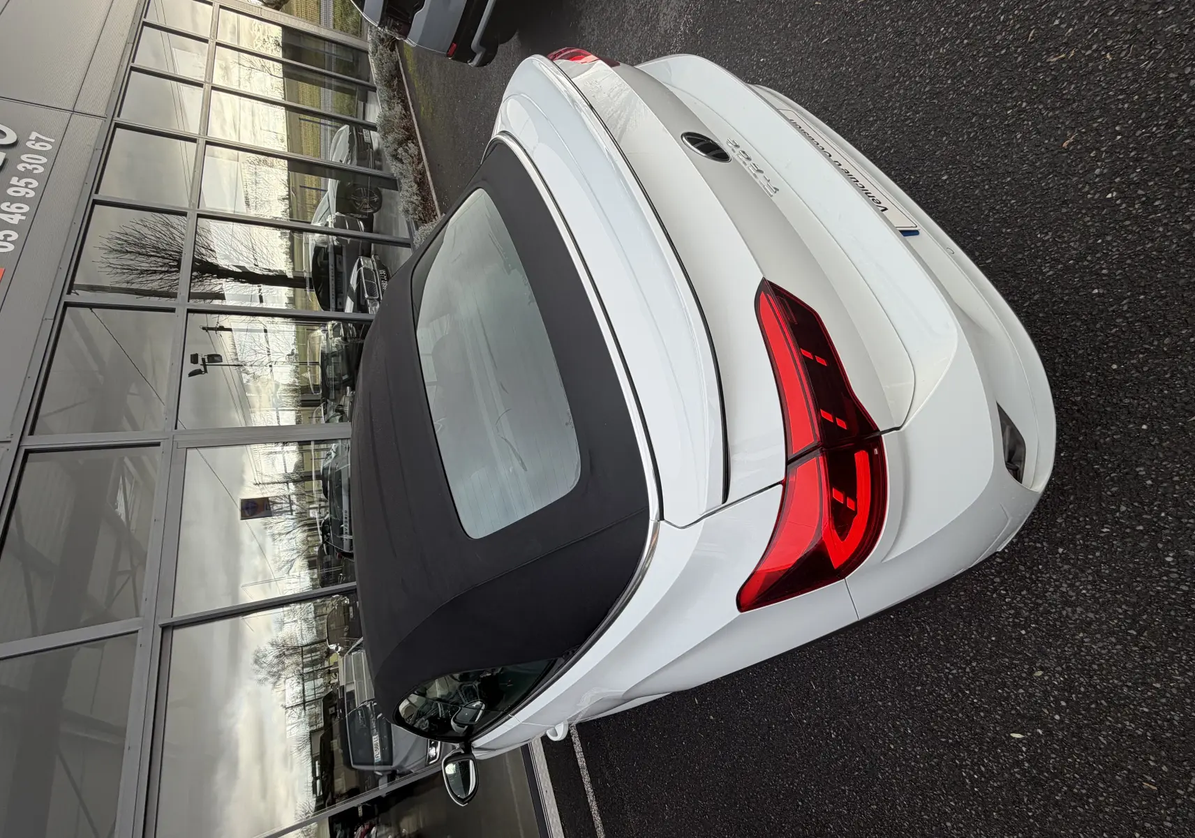 Vue 3/4 arrière d'un Volkswagen T-Roc Cabriolet blanc avec toit souple noir, feux arrière LED et finition R-Line.