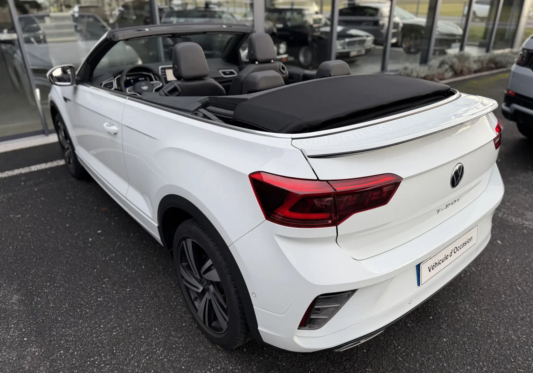 Vue 3/4 arrière droite du cabriolet Volkswagen T-Roc blanc avec toit souple noir partiellement ouvert et finition R-Line.