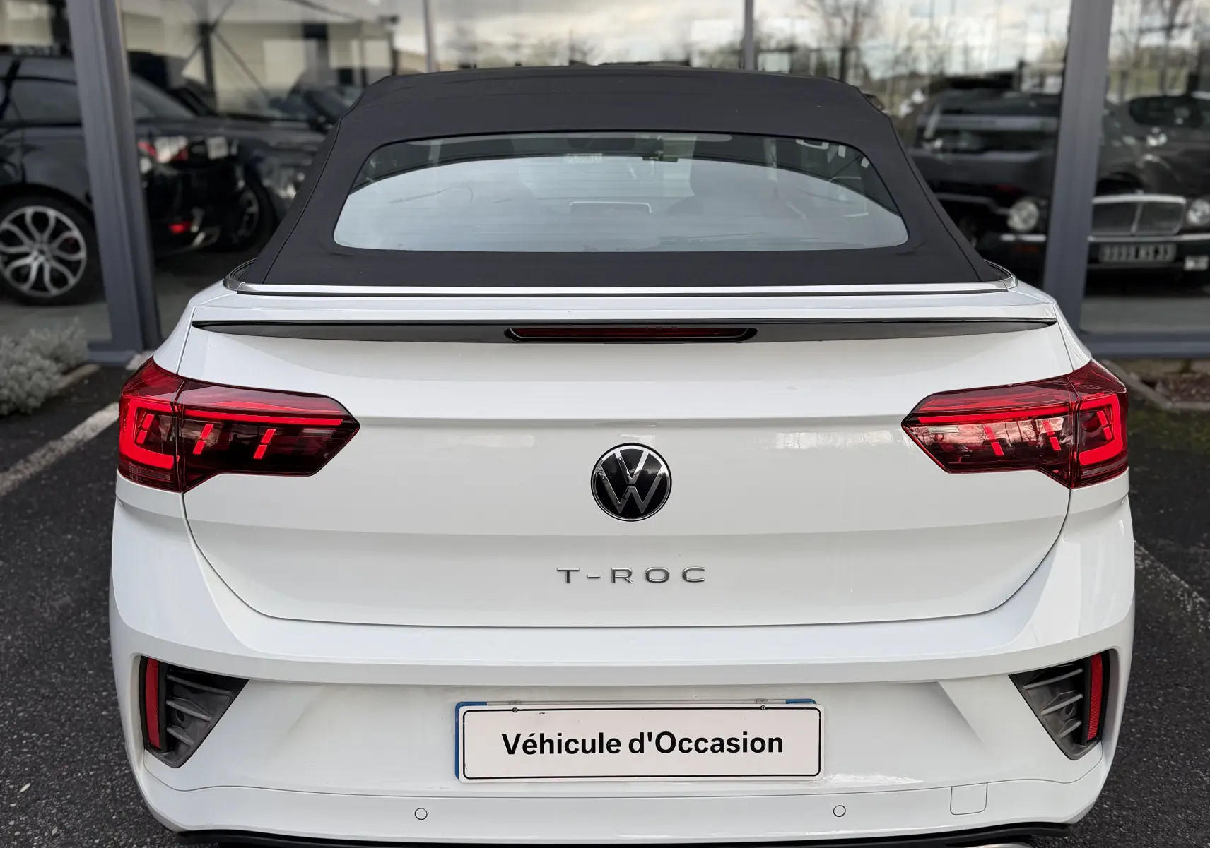 Vue arrière d’un Volkswagen T-Roc Cabriolet blanc 2022 avec toit noir fermé et feux arrière LED allumés.
