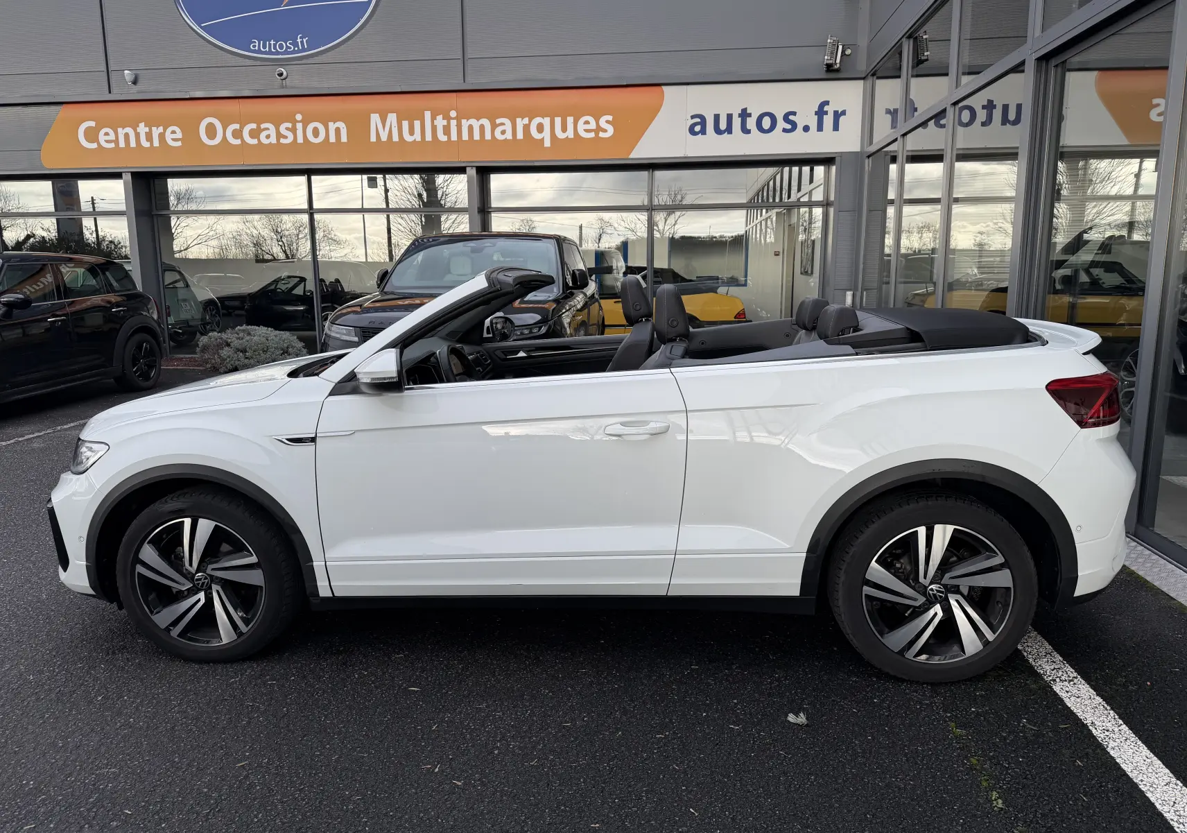 Vue de profil côté gauche d’un Volkswagen T-Roc Cabriolet blanc 2022 avec capote ouverte et jantes R-Line distinctives.
