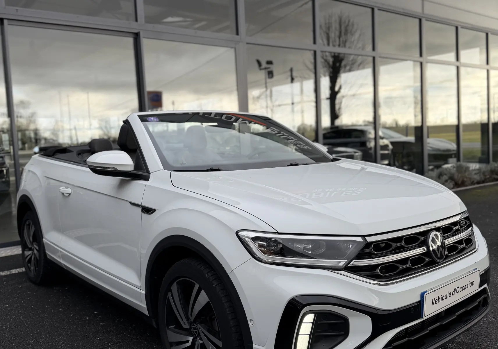 Volkswagen T-Roc Cabriolet blanc en 3/4 avant, capote ouverte, avec détails R-Line et feux LED allumés.