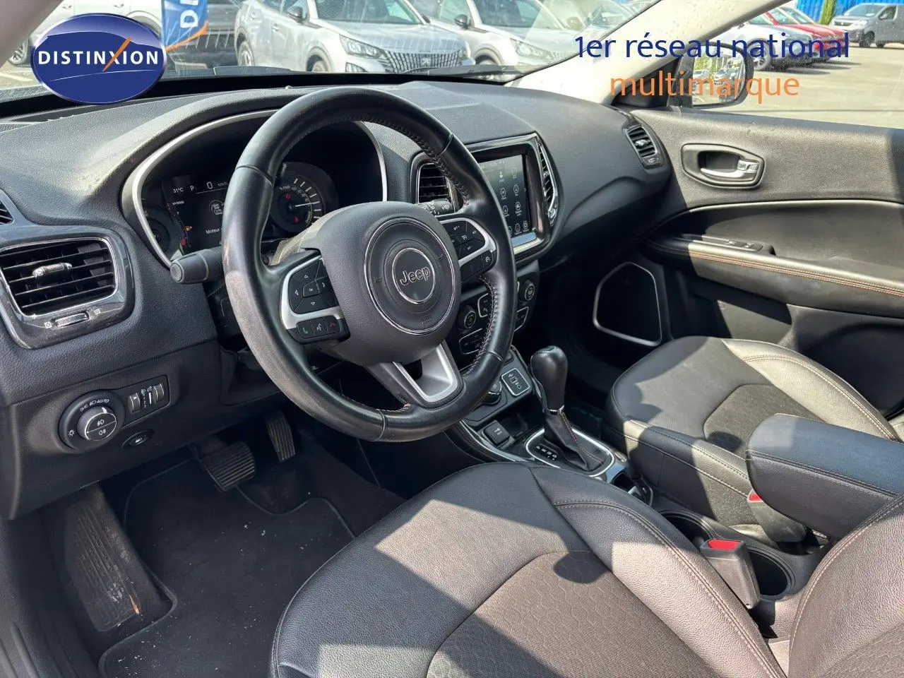 Vue intérieure avant droite du Jeep Compass blanc 2021, volant cuir, console centrale avec boîte auto et écran tactile.