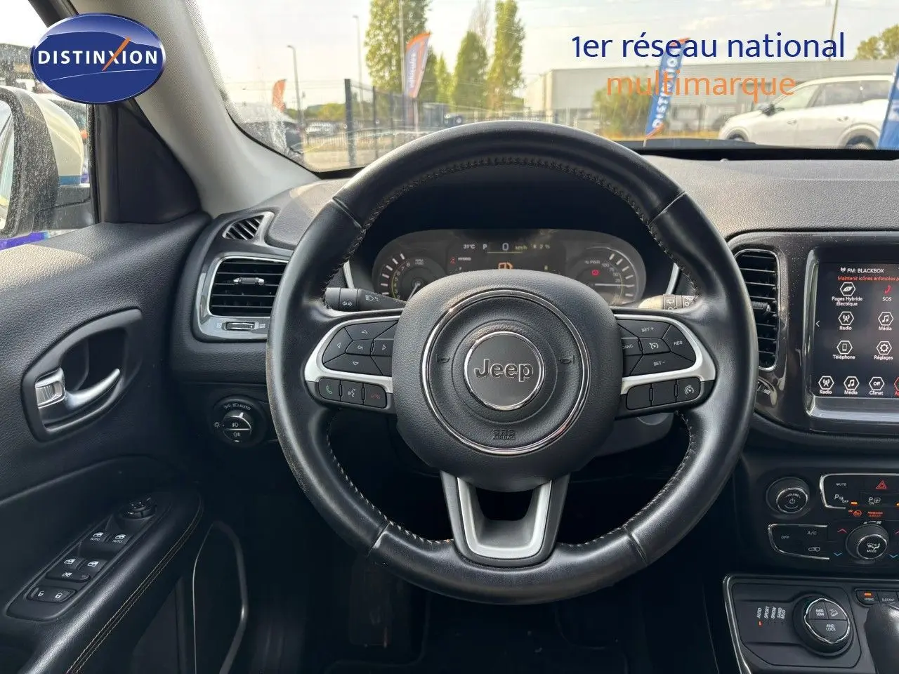 Vue intérieure centrée sur le volant Jeep noir, tableau de bord digital et écran tactile du Compass blanc hybride rechargeable.