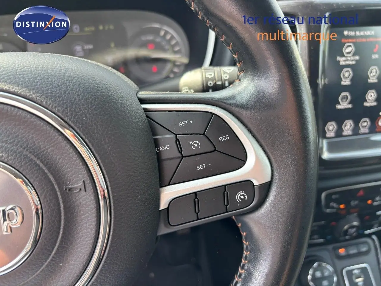 Gros plan sur le volant cuir noir du Jeep Compass 2021 avec commandes de régulateur de vitesse et tableau de bord flou.