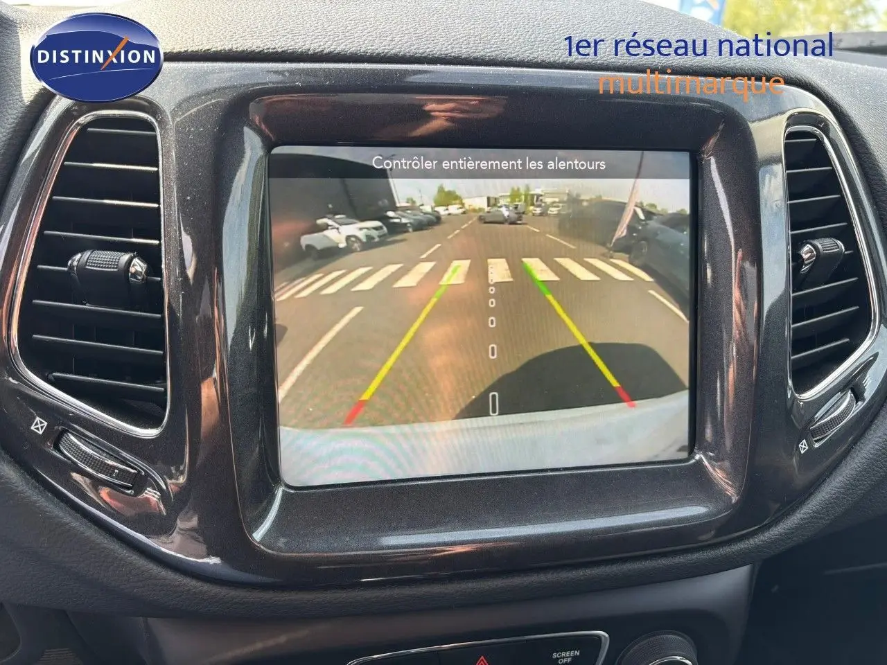 Écran central du Jeep Compass blanc montrant la caméra de recul avec lignes de guidage colorées.