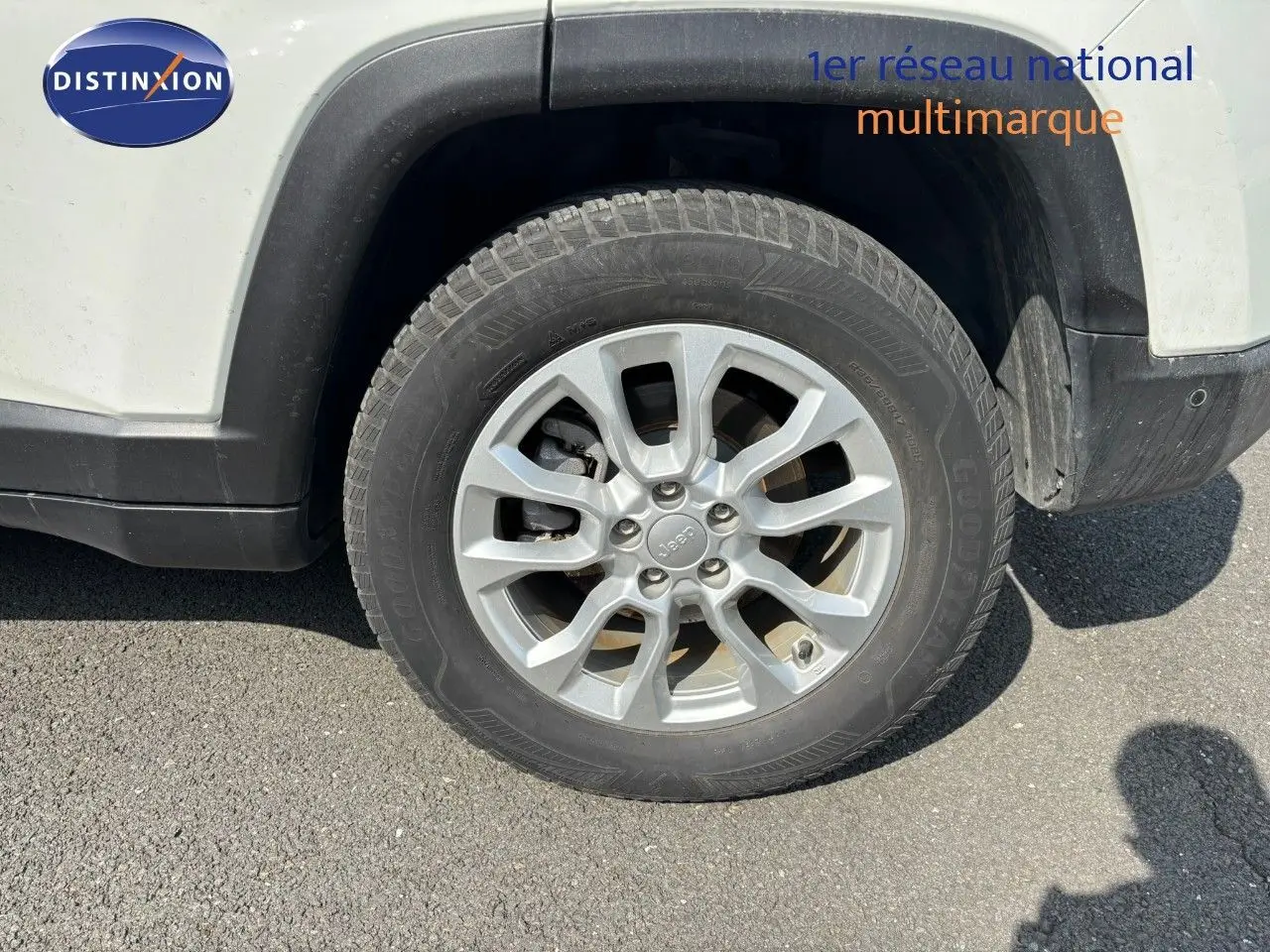 Gros plan sur la roue avant droite d’un Jeep Compass blanc, avec jante alliage argentée et pneu Goodyear.