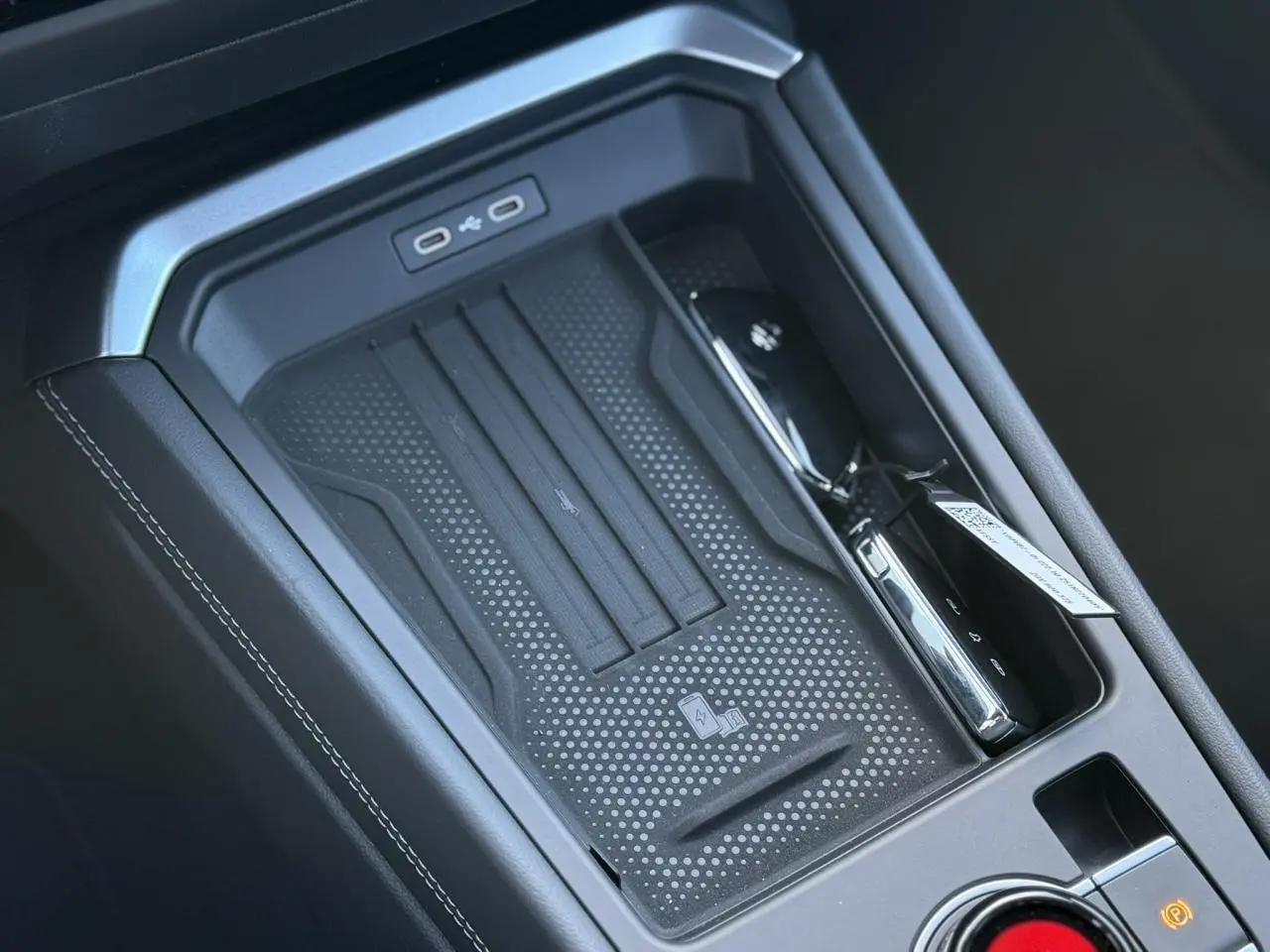 Gros plan sur la console centrale noire du Volkswagen T-Roc 2026 avec zone de charge sans fil et ports USB-C.