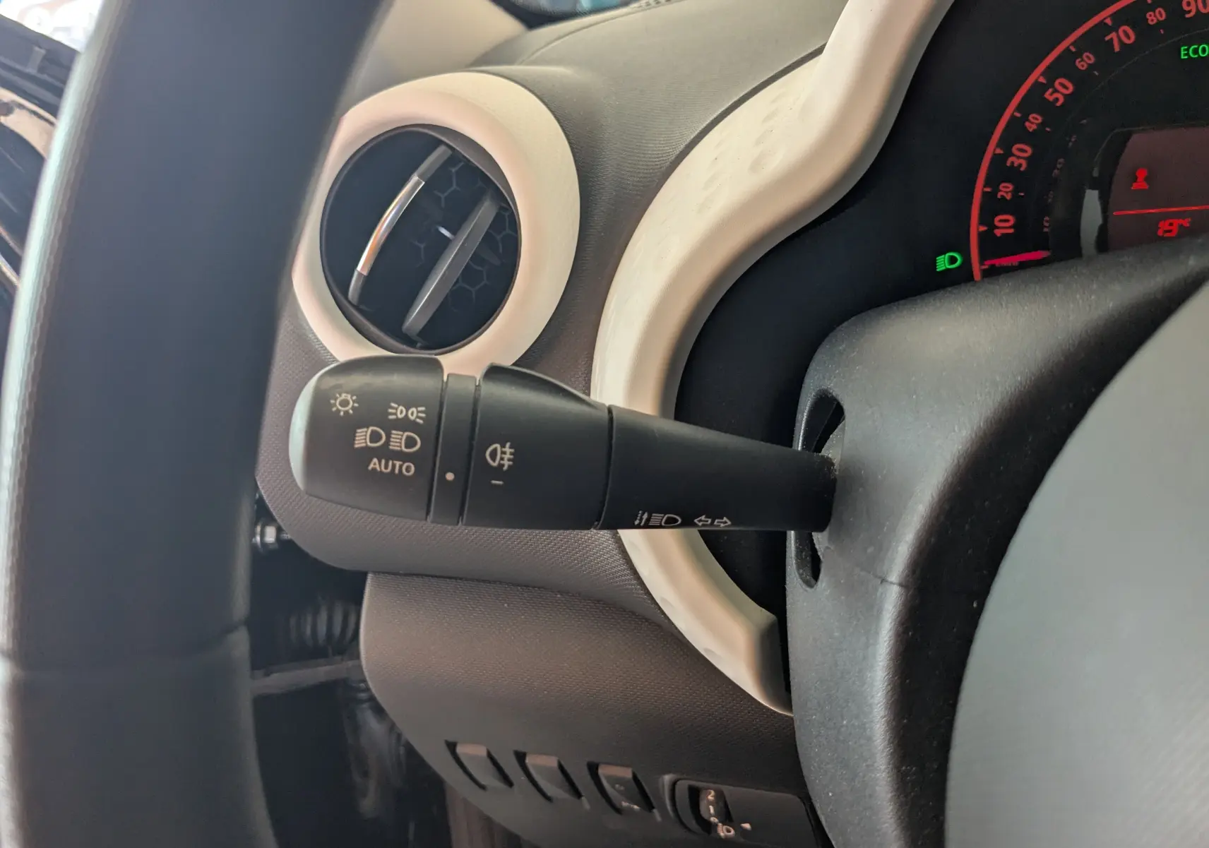 Gros plan sur la commande des feux et clignotants à gauche du volant dans l’habitacle gris clair d’une Renault Twingo III noire.