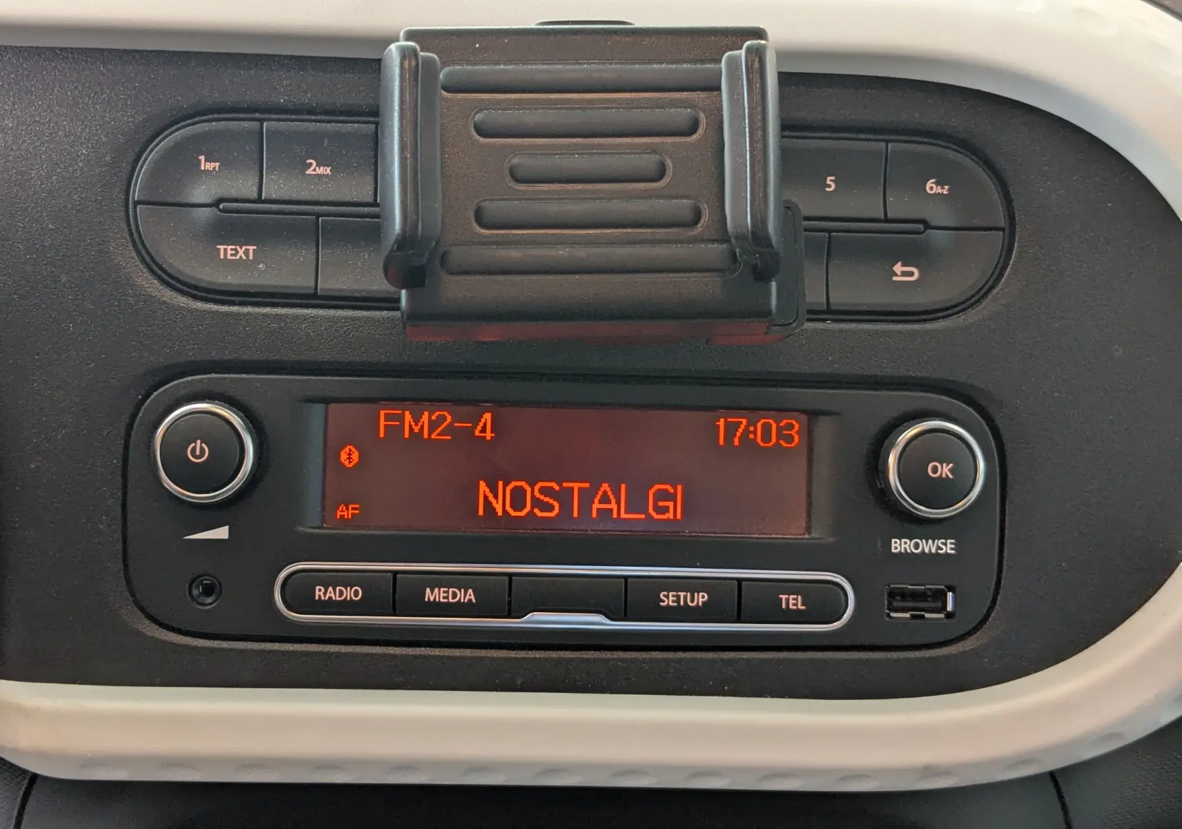 Détail du tableau de bord de la Renault Twingo III noir, affichant l’autoradio avec la station Nostalgie à 17h03.