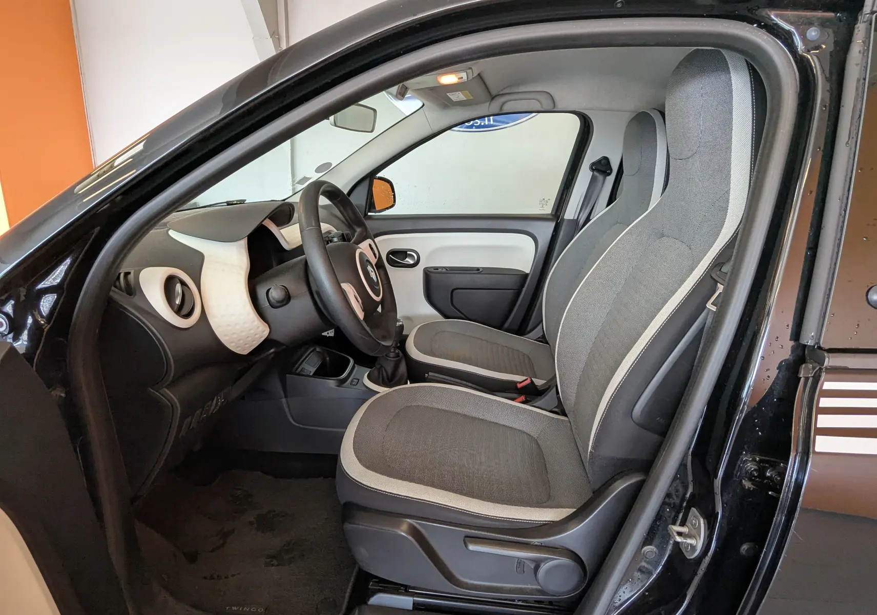 Vue intérieure côté conducteur de la Renault Twingo III noire, montrant les sièges gris et le tableau de bord clair.