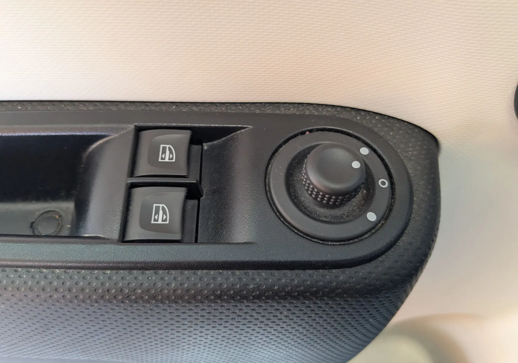 Gros plan sur les commandes de lève-vitres et réglage des rétroviseurs côté conducteur d'une Renault Twingo III noire.