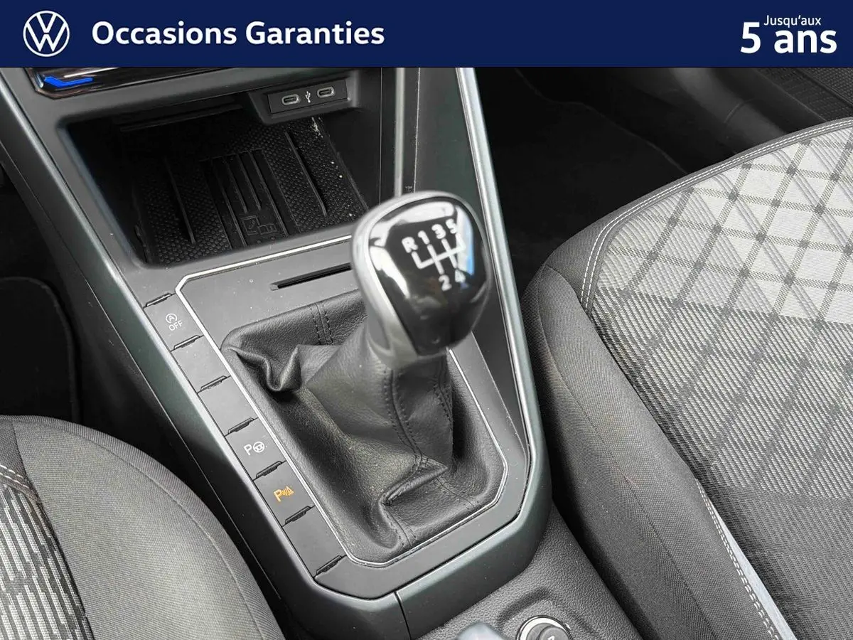 Le levier de vitesses manuel noir de la Volkswagen Polo 2025, avec console centrale et siège avant gris à motifs.
