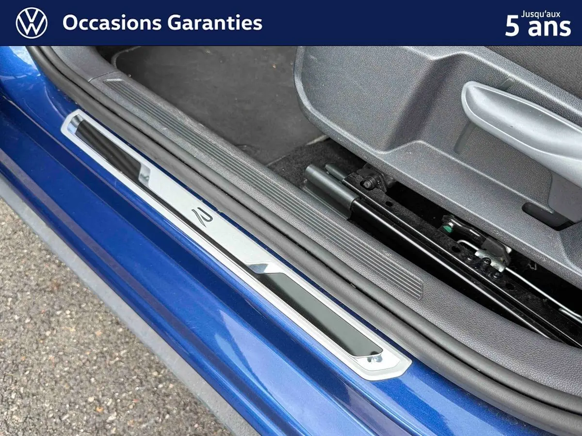 Détail de la porte côté conducteur d’une Volkswagen Polo bleue métallisée avec seuil de porte en métal et intérieur gris.