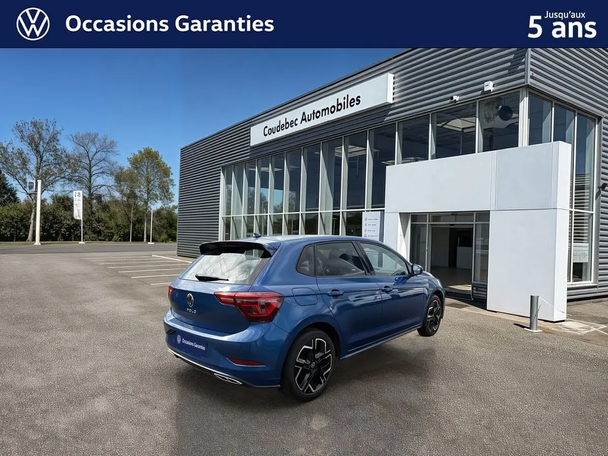 Volkswagen Polo bleue vue 3/4 arrière droit, avec toit noir et jantes alliage 17 pouces devant un concessionnaire.