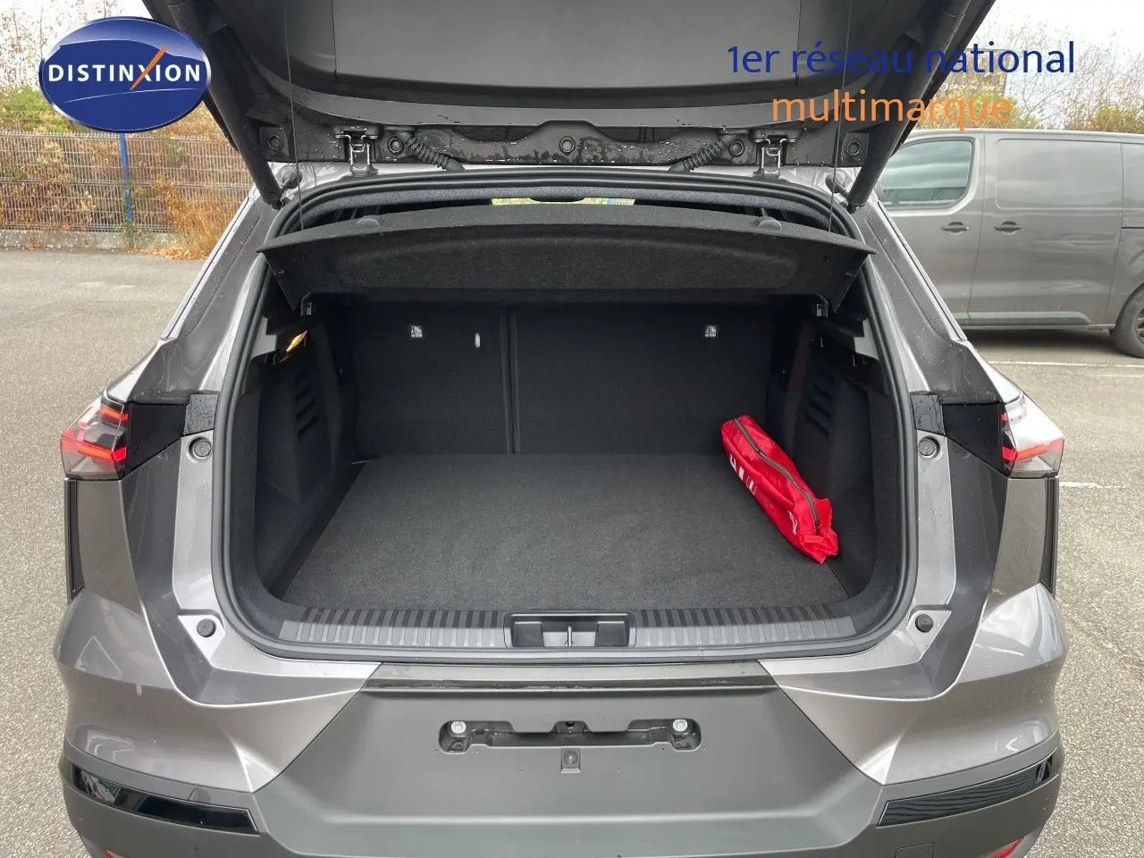 Vue arrière du coffre ouvert d'une Renault Symbioz gris cassiopée métal, avec un kit de sécurité rouge à l'intérieur.