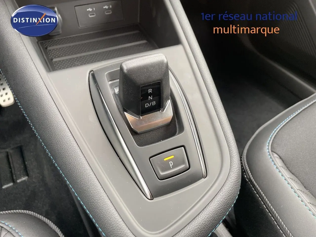Le levier de vitesses automatique noir et gris du Renault Symbioz 2026, entouré de coutures bleues sur la console centrale.