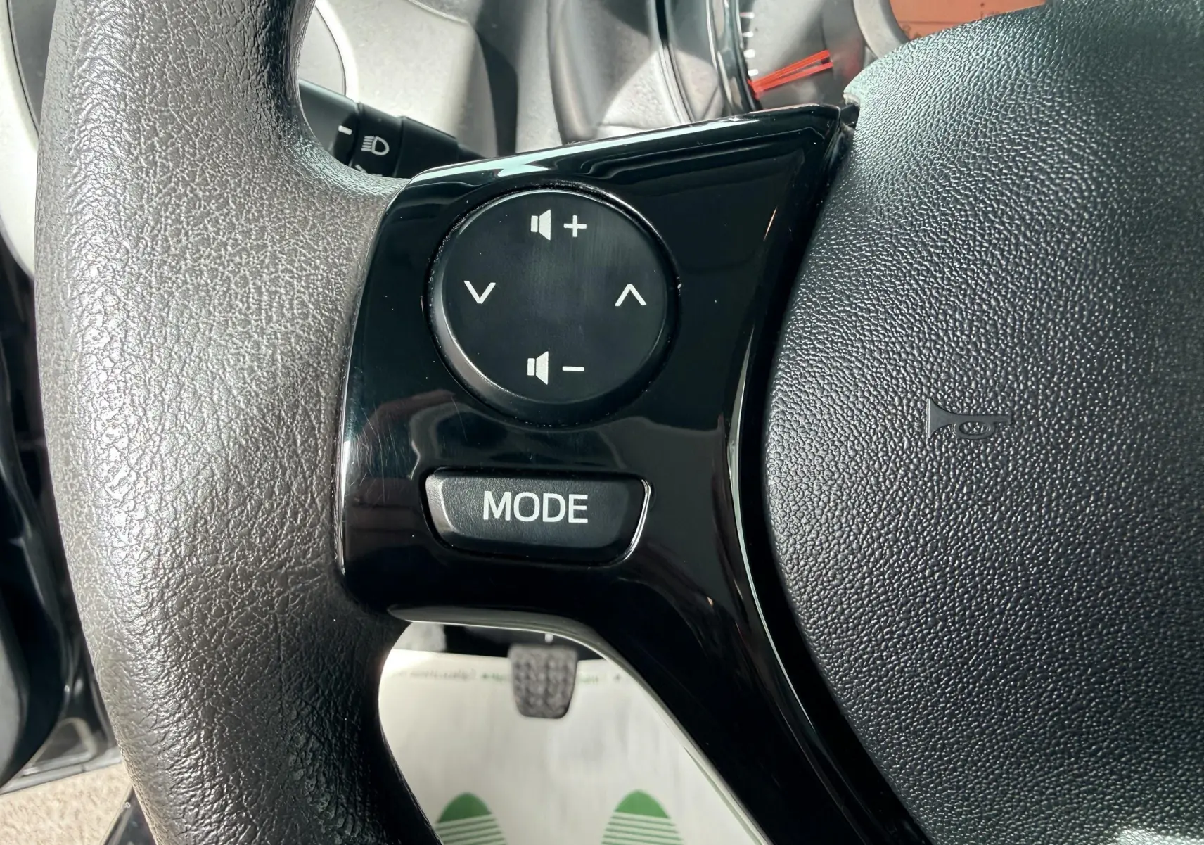 Gros plan sur les commandes audio noires du volant d'une Peugeot 108 2018, avec tableau de bord en arrière-plan.