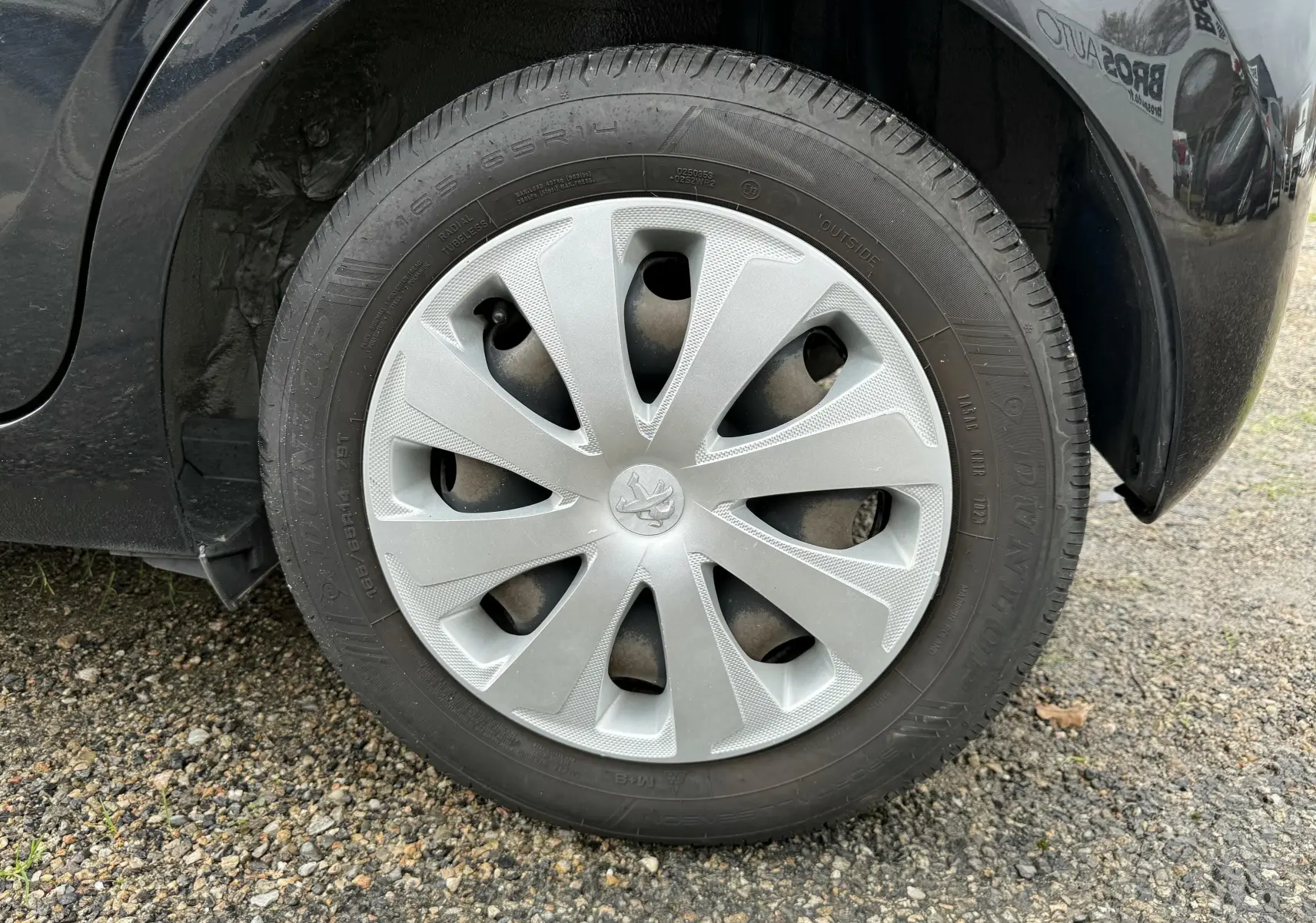 Gros plan sur la roue avant gauche noire d'une Peugeot 108 2018 avec enjoliveur argenté et logo lion au centre.