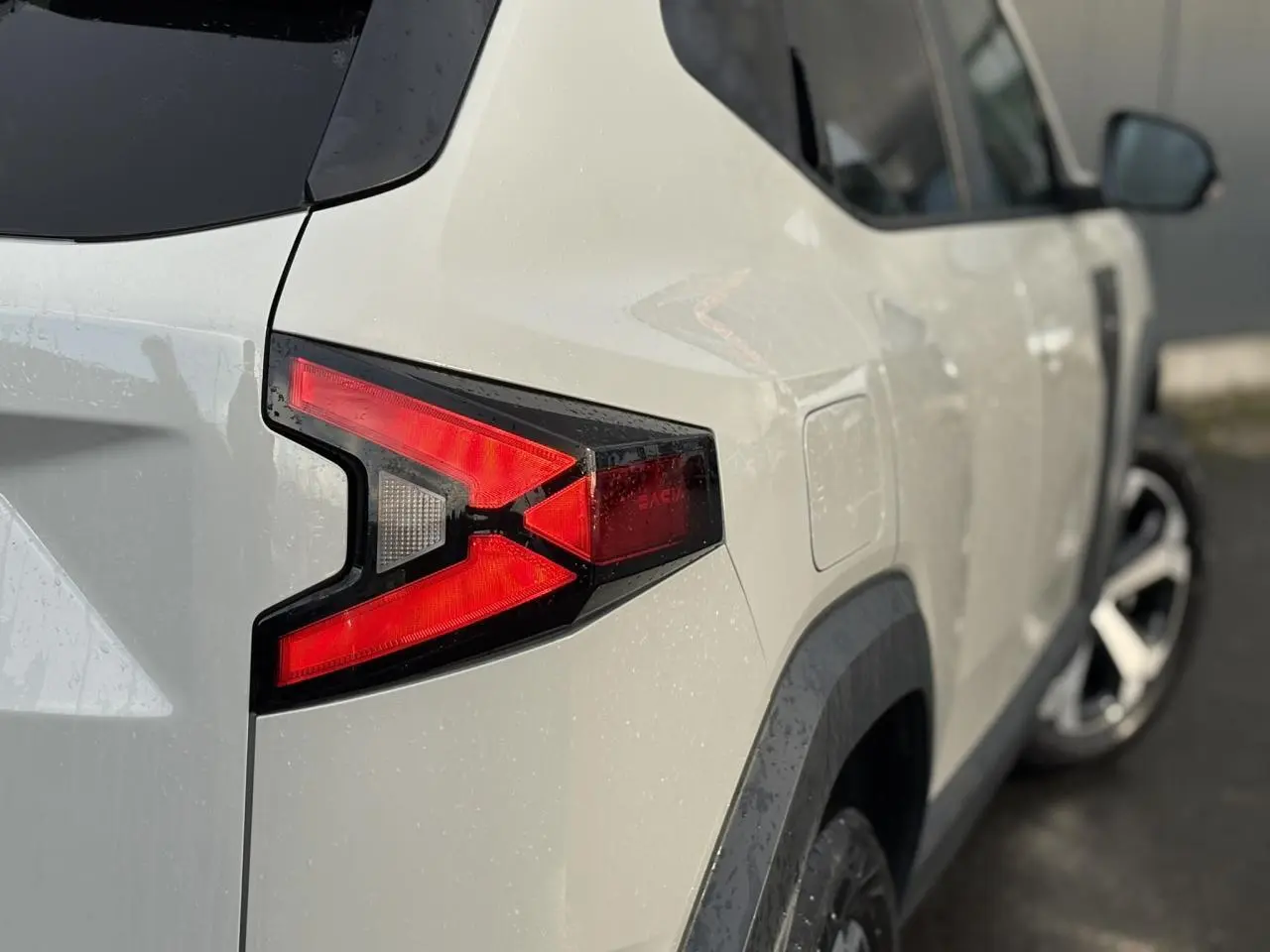 Vue arrière côté gauche du Dacia Duster 2024 beige Sandstone avec feux arrière LED en forme de flèche.