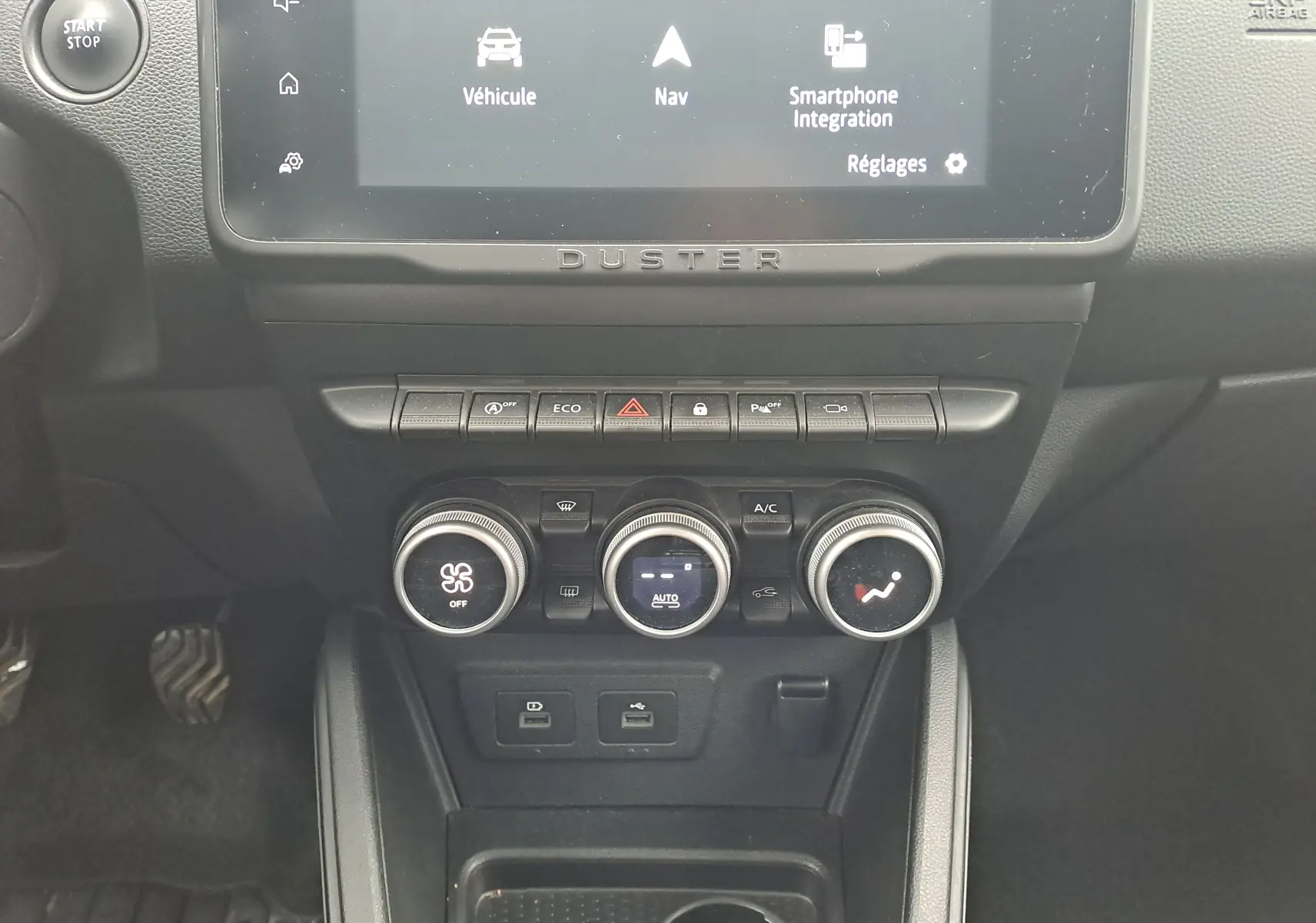 Vue rapprochée du tableau de bord noir du Dacia Duster 2023, avec commandes climatisation et écran tactile affichant la navigation.