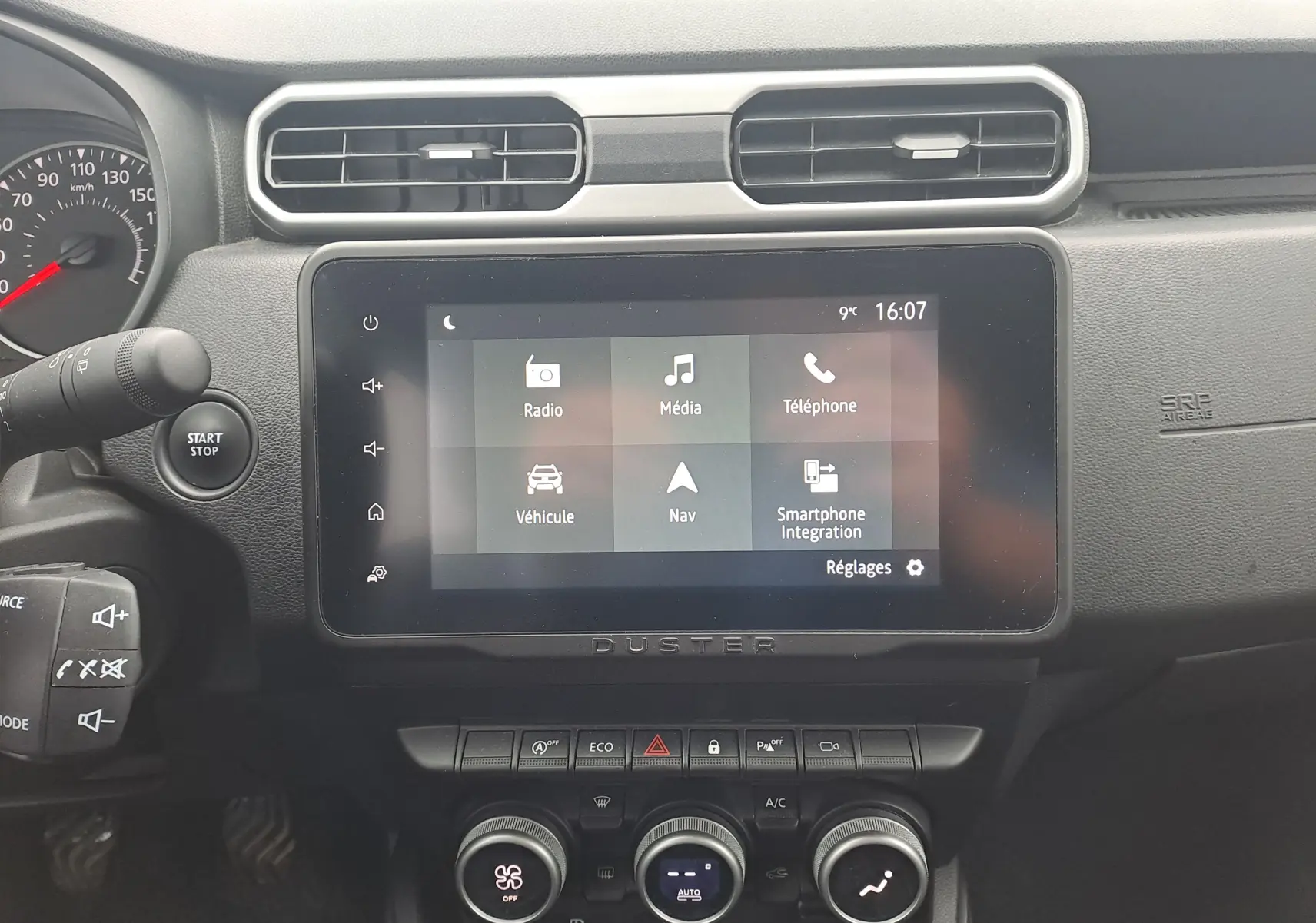 Vue rapprochée de l’écran tactile central et du tableau de bord noir du Dacia Duster 2023, avec commandes climatisation et bouton start/stop.
