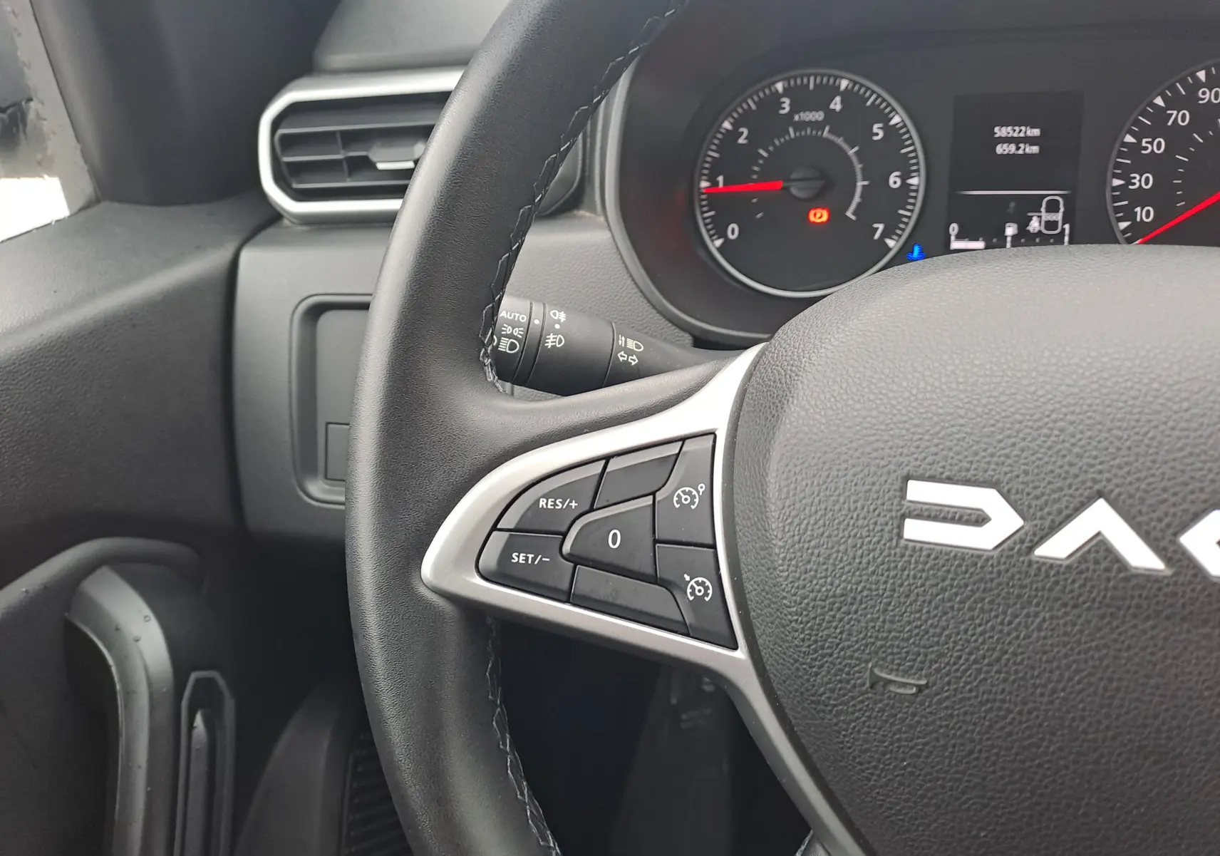 Gros plan sur le volant noir du Dacia Duster 2023, montrant les commandes de régulateur de vitesse et le tableau de bord en arrière-plan.