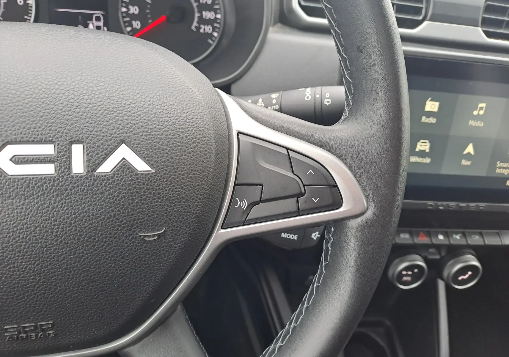 Gros plan sur le volant noir de la Dacia Duster 2023, avec commandes audio et tableau de bord en arrière-plan.