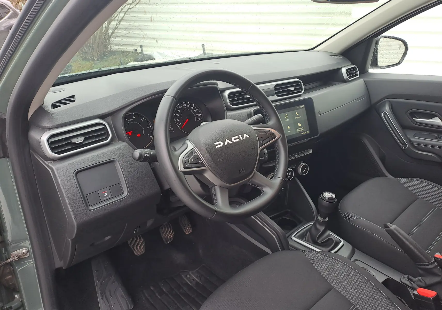 Vue intérieure côté conducteur du Dacia Duster 2023 kaki Liken, volant multifonction et boîte manuelle visibles.