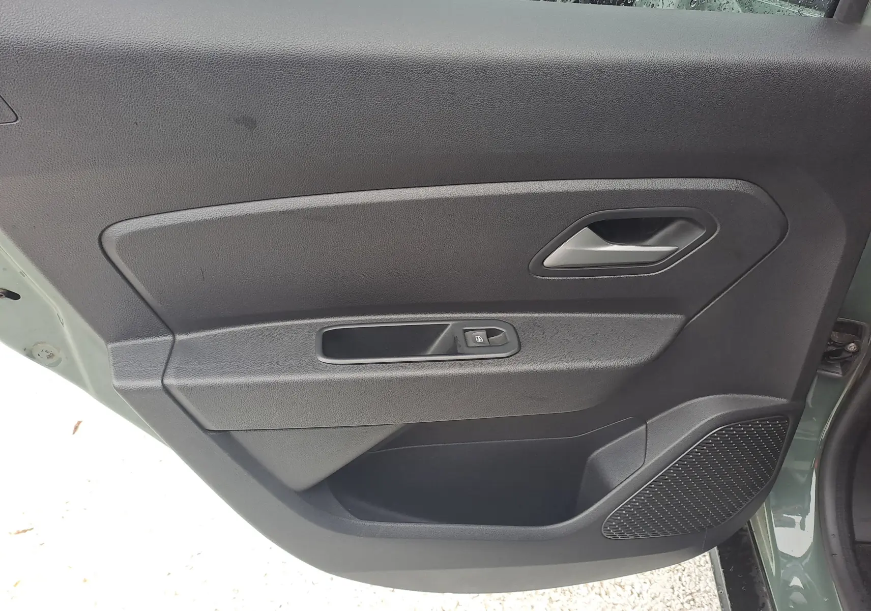 Vue intérieure de la porte arrière gauche du Dacia Duster 2023 kaki avec commande de vitre et haut-parleur intégré.