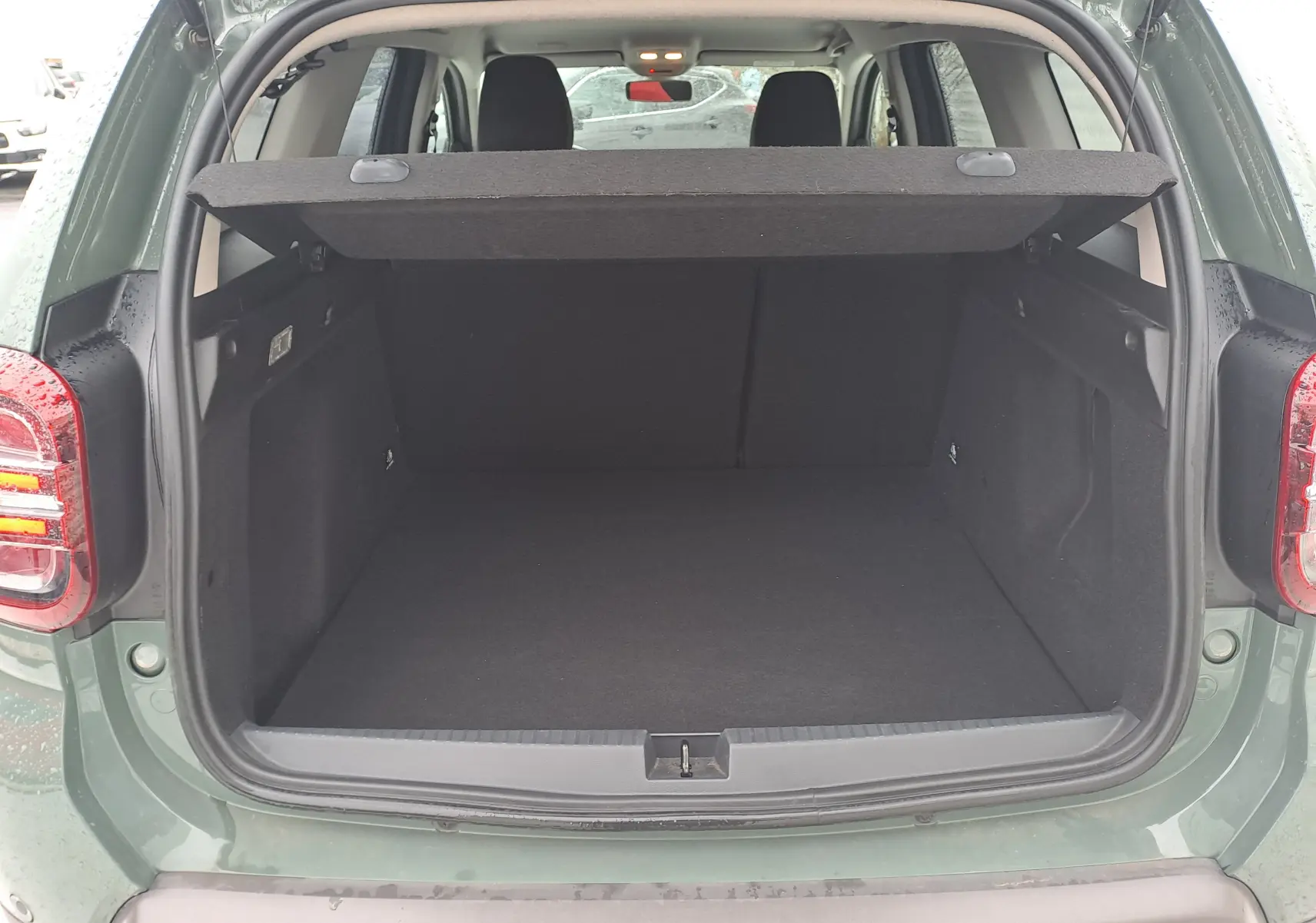 Vue arrière du coffre ouvert d'un Dacia Duster 2023 kaki Liken, montrant l'espace de chargement vide et la tablette cache-bagages.
