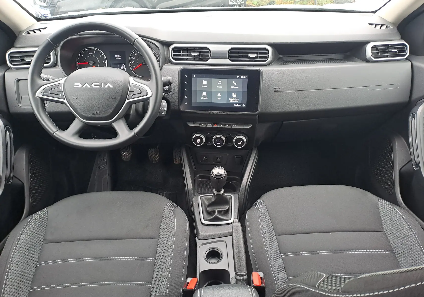 Vue intérieure avant du Dacia Duster 2023, tableau de bord noir avec volant multifonction et boîte manuelle.