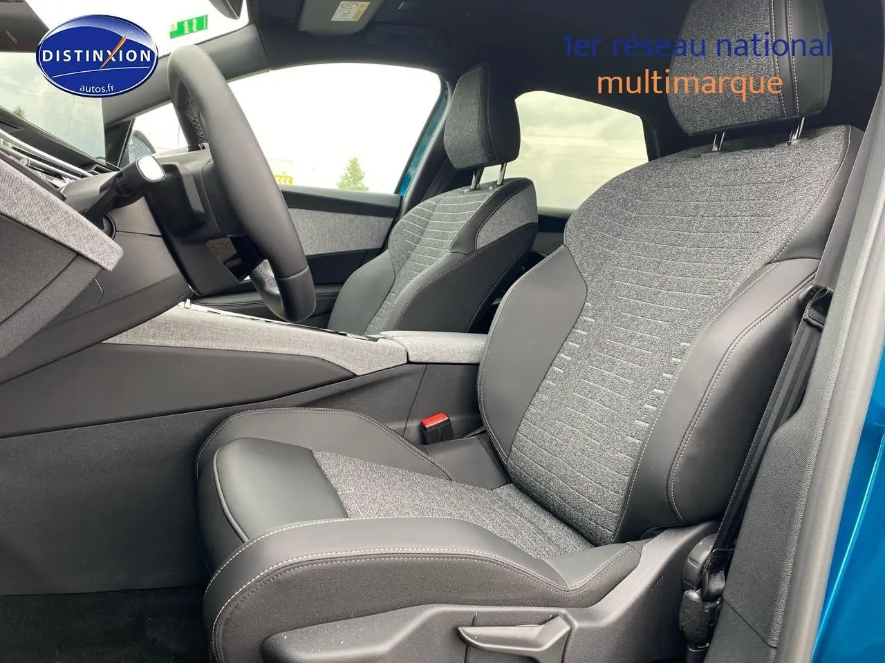 Vue intérieure côté conducteur du Peugeot 3008 bleu 2025, sièges tissu et cuir gris avec accoudoir central.