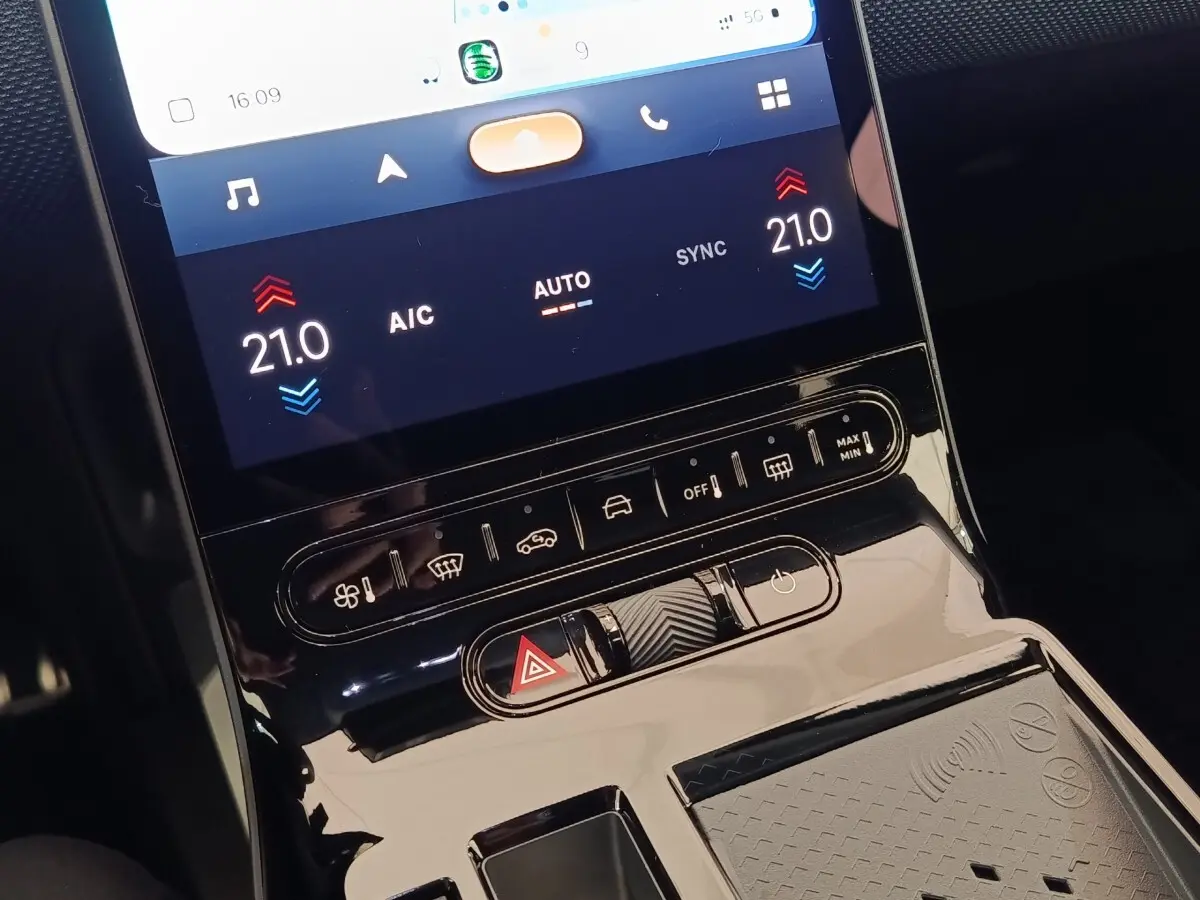 Gros plan sur la console centrale tactile noire du Citroën C5 hybride avec commandes climatisation et recharge sans fil.