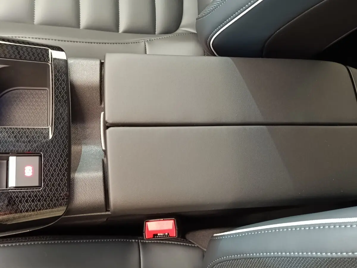 Détail de l'accoudoir central noir et console avec bouton frein électrique dans l'habitacle d'une Citroën C5 Hybride.