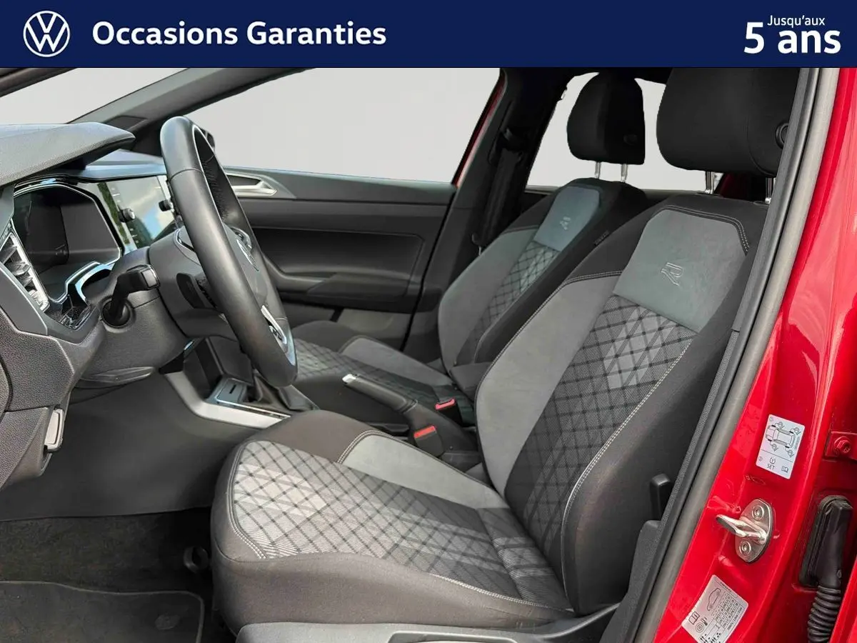 Vue intérieure côté conducteur de la Volkswagen Polo rouge 2025, sièges tissu gris avec surpiqûres et volant cuir.