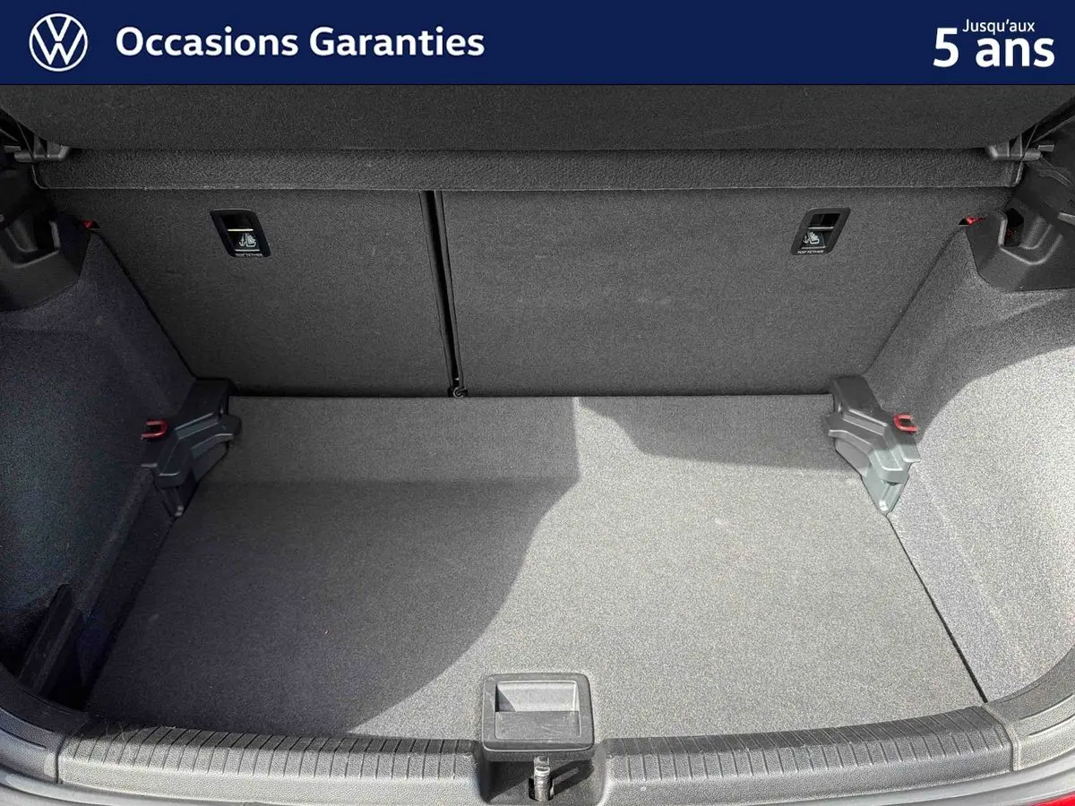 Coffre ouvert de la Volkswagen Polo rouge, vue arrière montrant l’espace de chargement vide et la moquette grise.