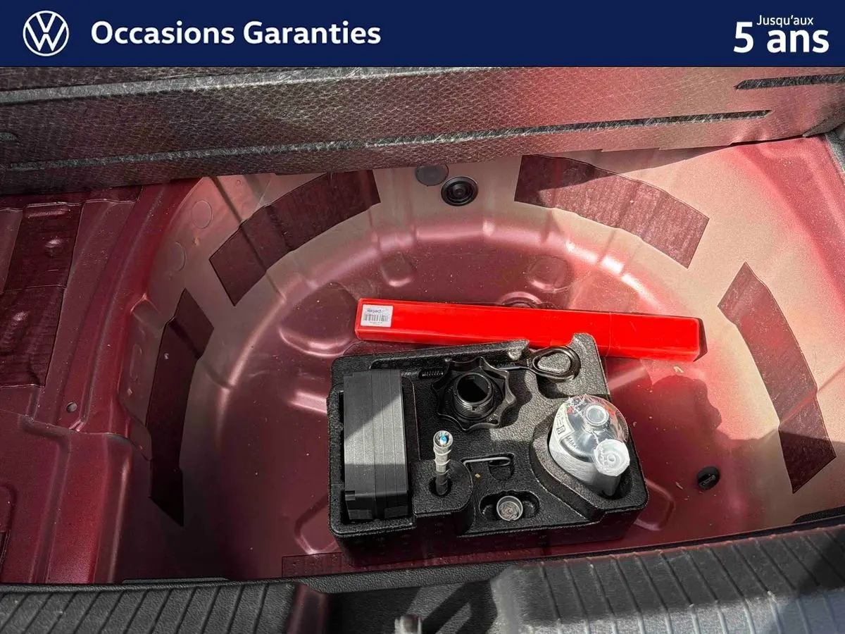 Vue rapprochée de la roue de secours rouge métallisée d’une Volkswagen Polo 2025 avec kit de réparation et triangle de signalisation.